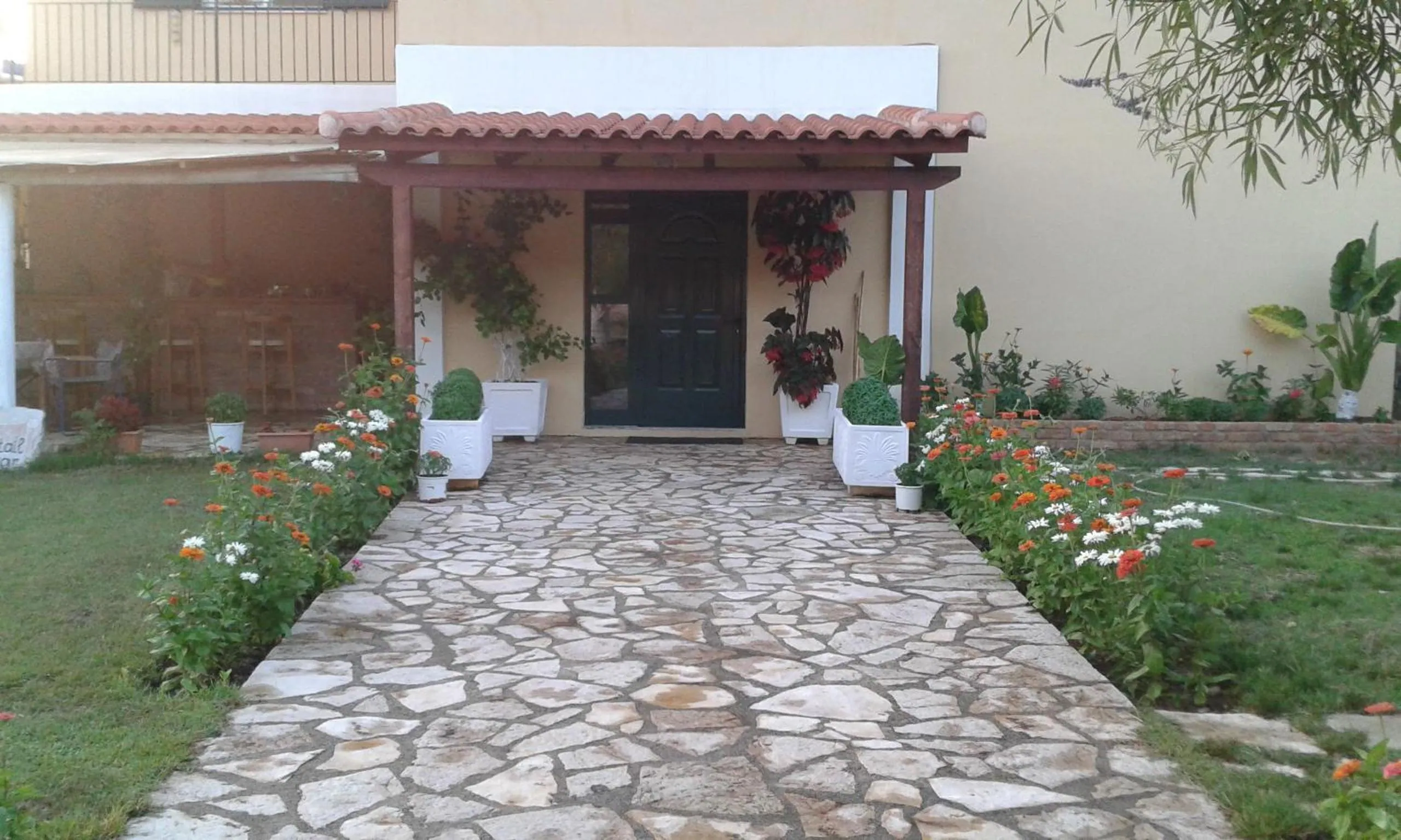 A flagstone path between flower beds leading to the green front door under a tiled pergola