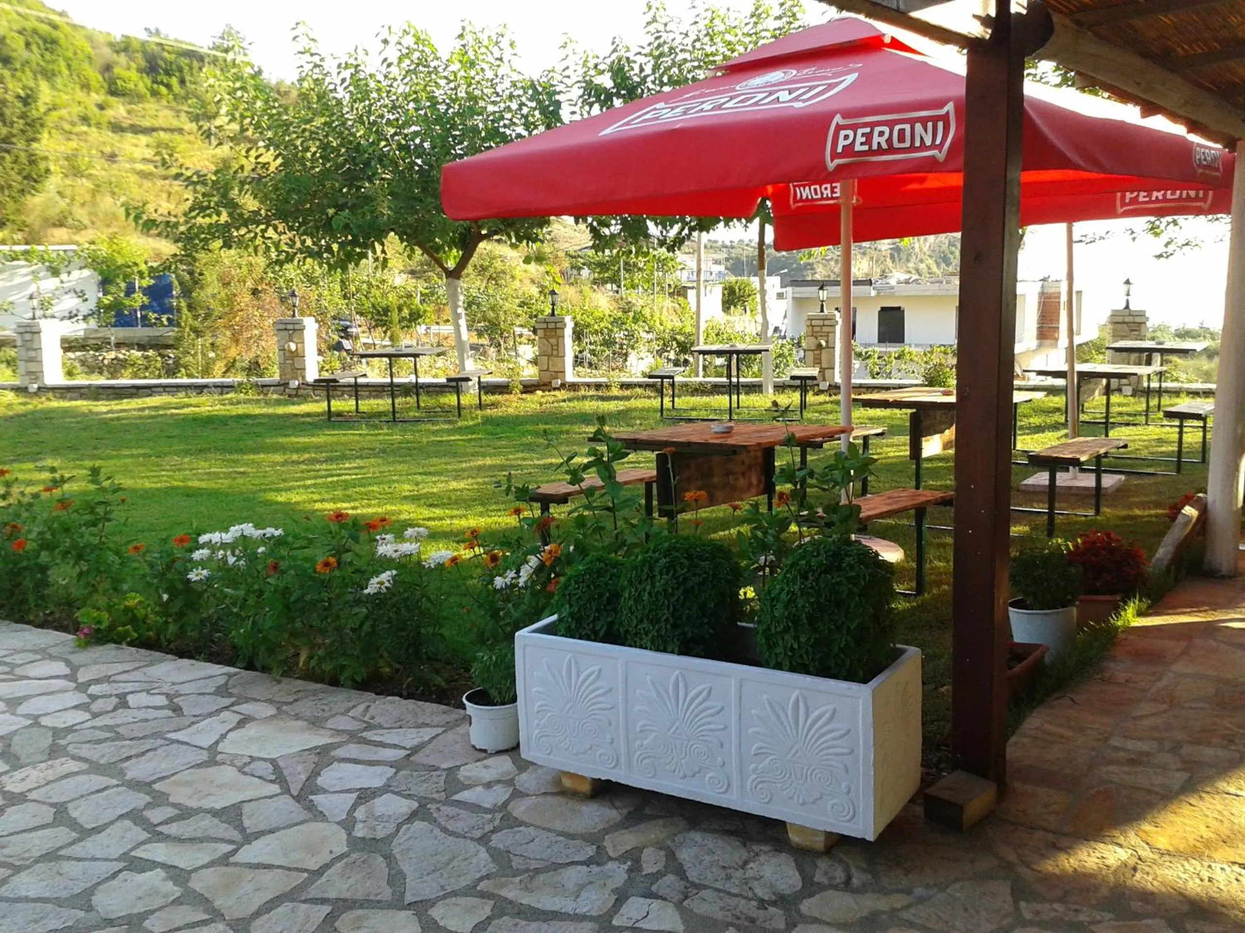 Garden tables under a red umbrella beside a white planter, with the lawn and fruit trees beyond