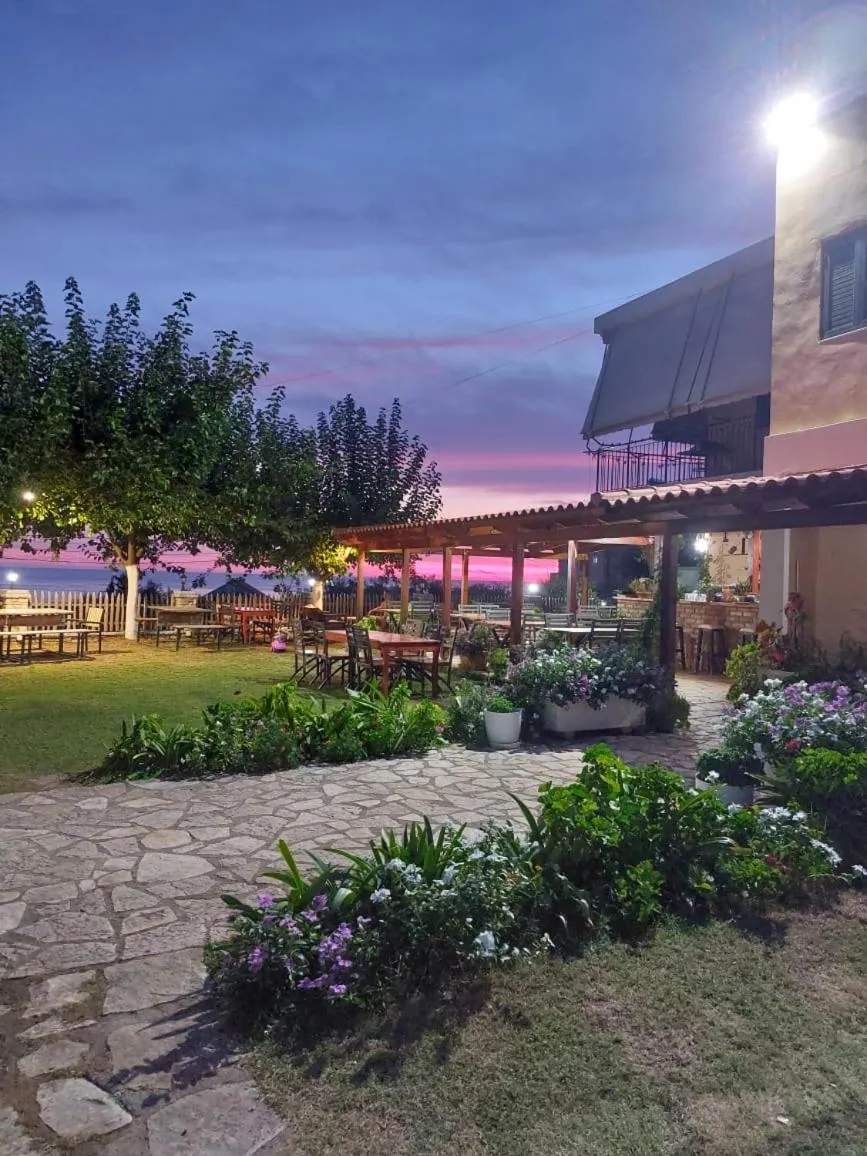 The pergola and its tables lit at dusk, the sky pink over the sea behind the plane trees
