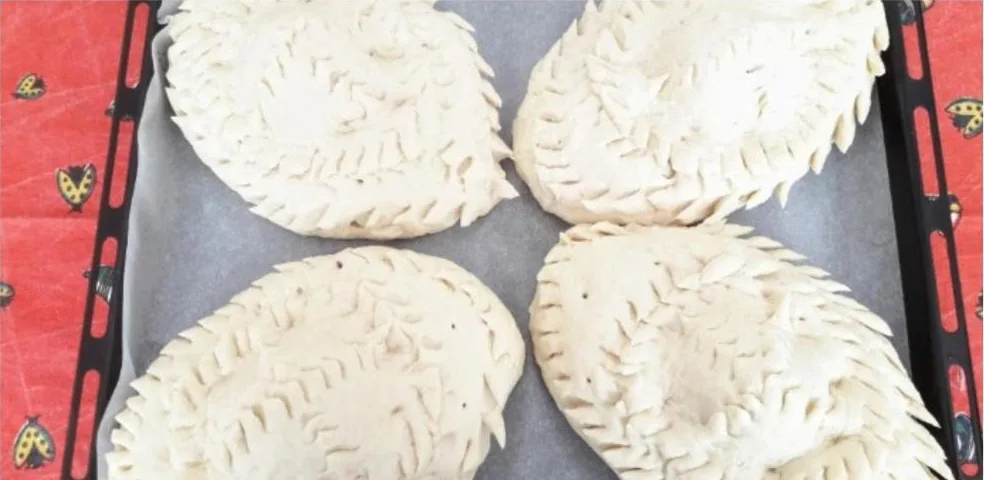 Four hand-crimped pies on a baking tray before they go into the oven