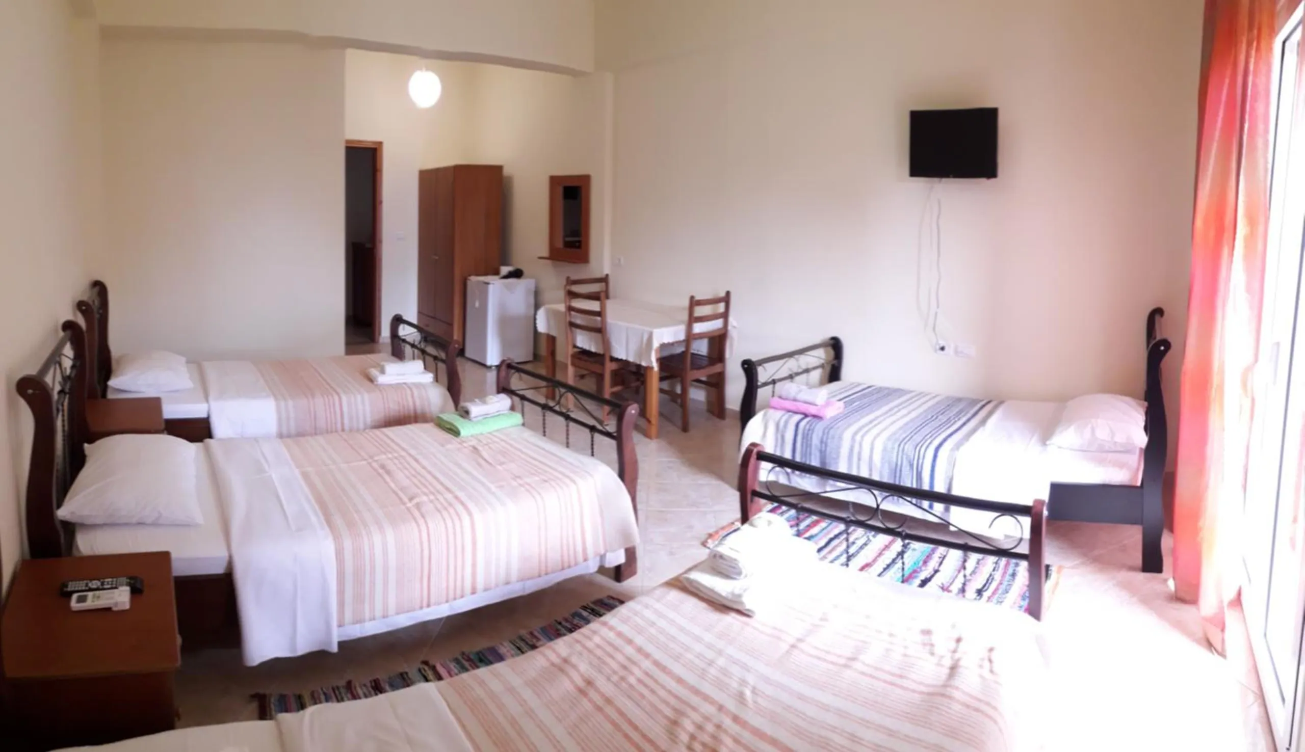 A wide view of a quadruple room with striped bedspreads, a wardrobe, a television and a table by the window
