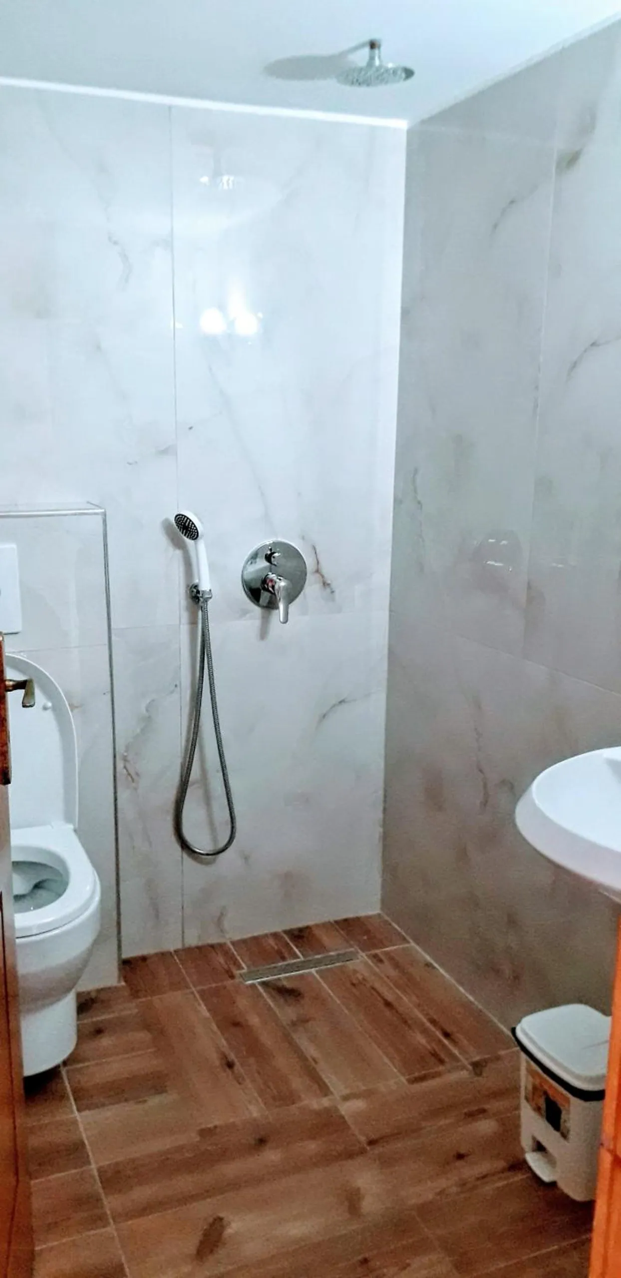 A shower room with marble-effect tiles, a rain shower head and a wood-effect floor
