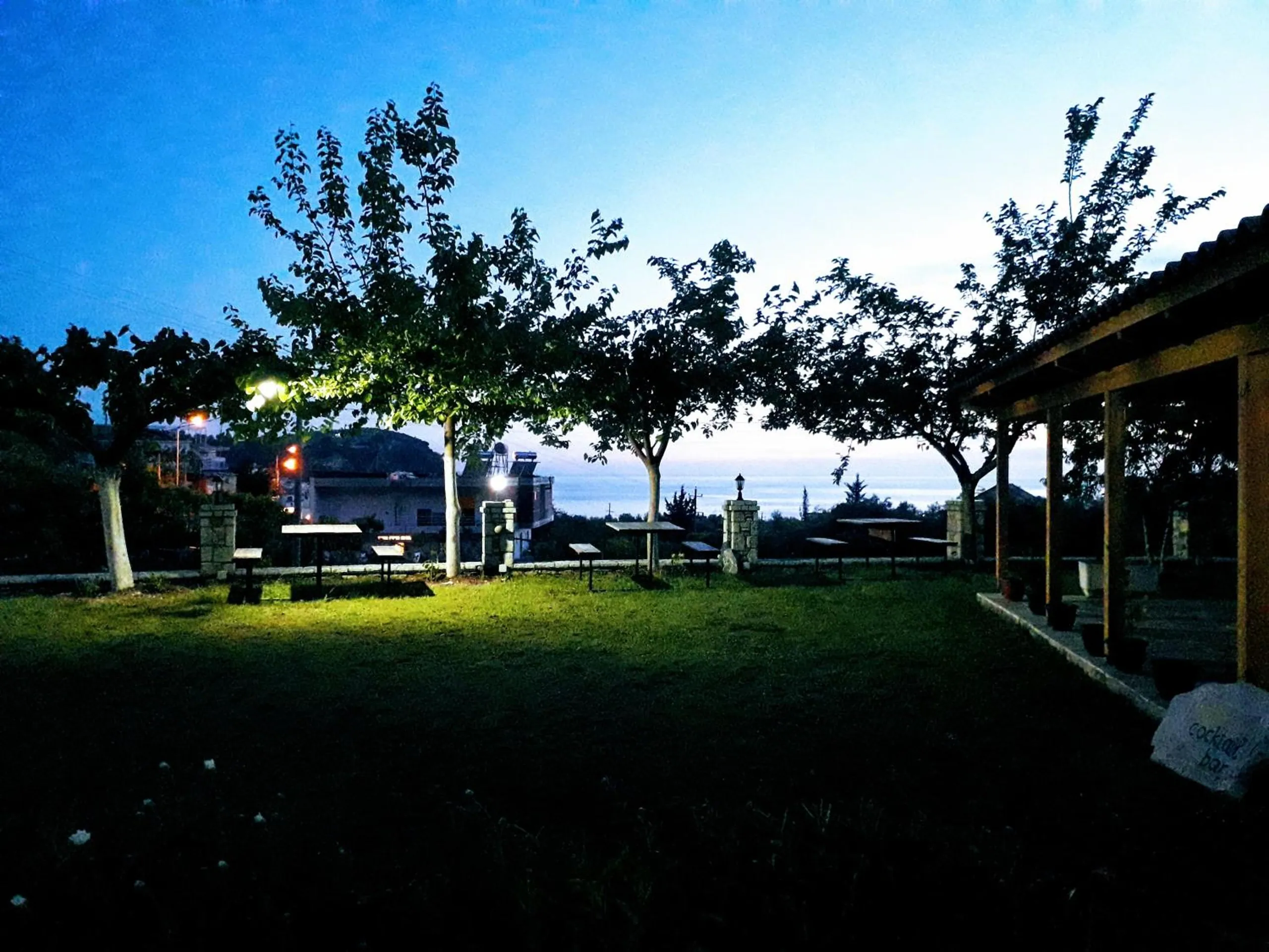 The lawn at nightfall with lamps on the stone gateposts and the lights of the bay beyond