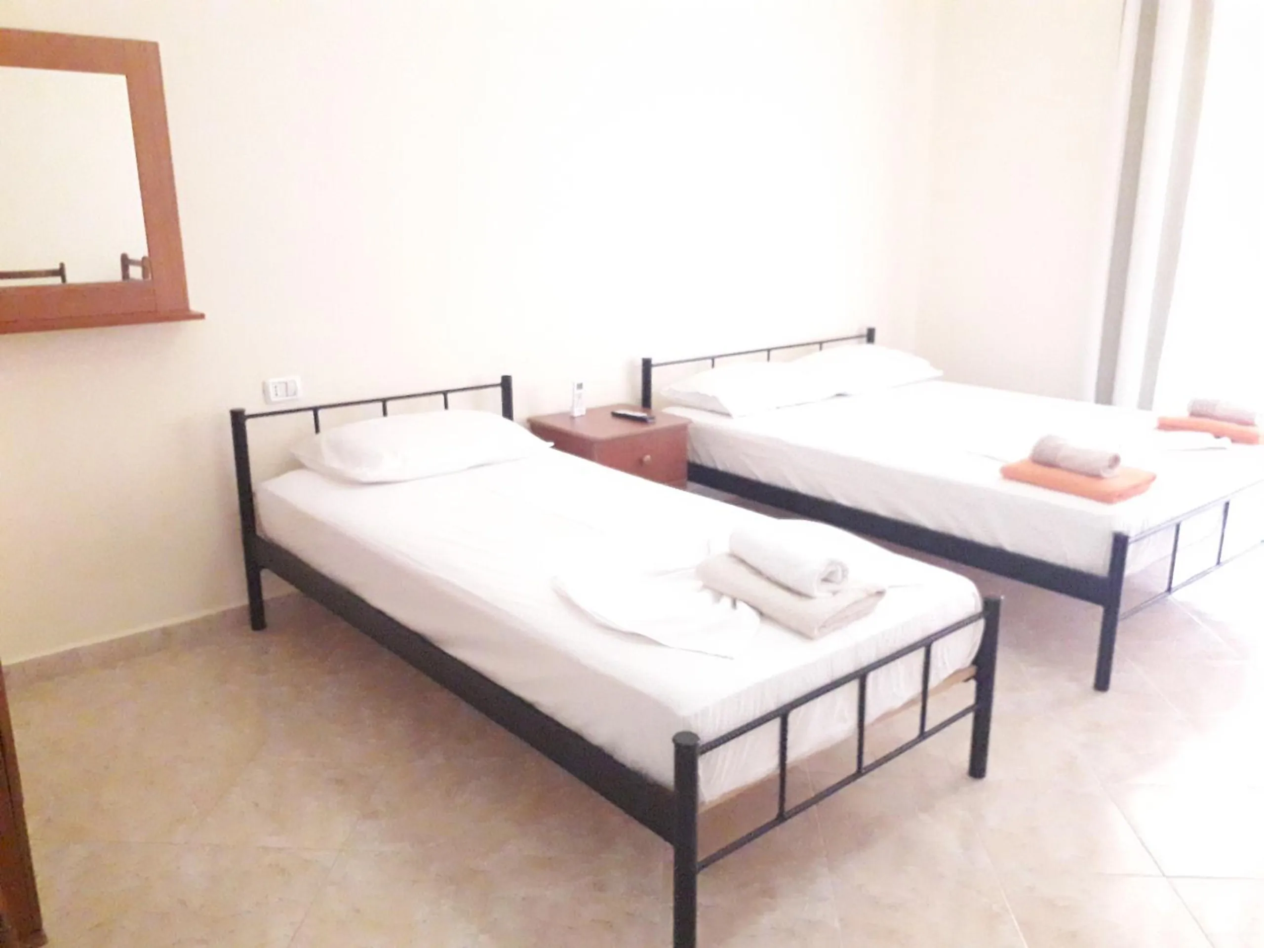Two single iron beds with folded towels and a wooden mirror in a bright room