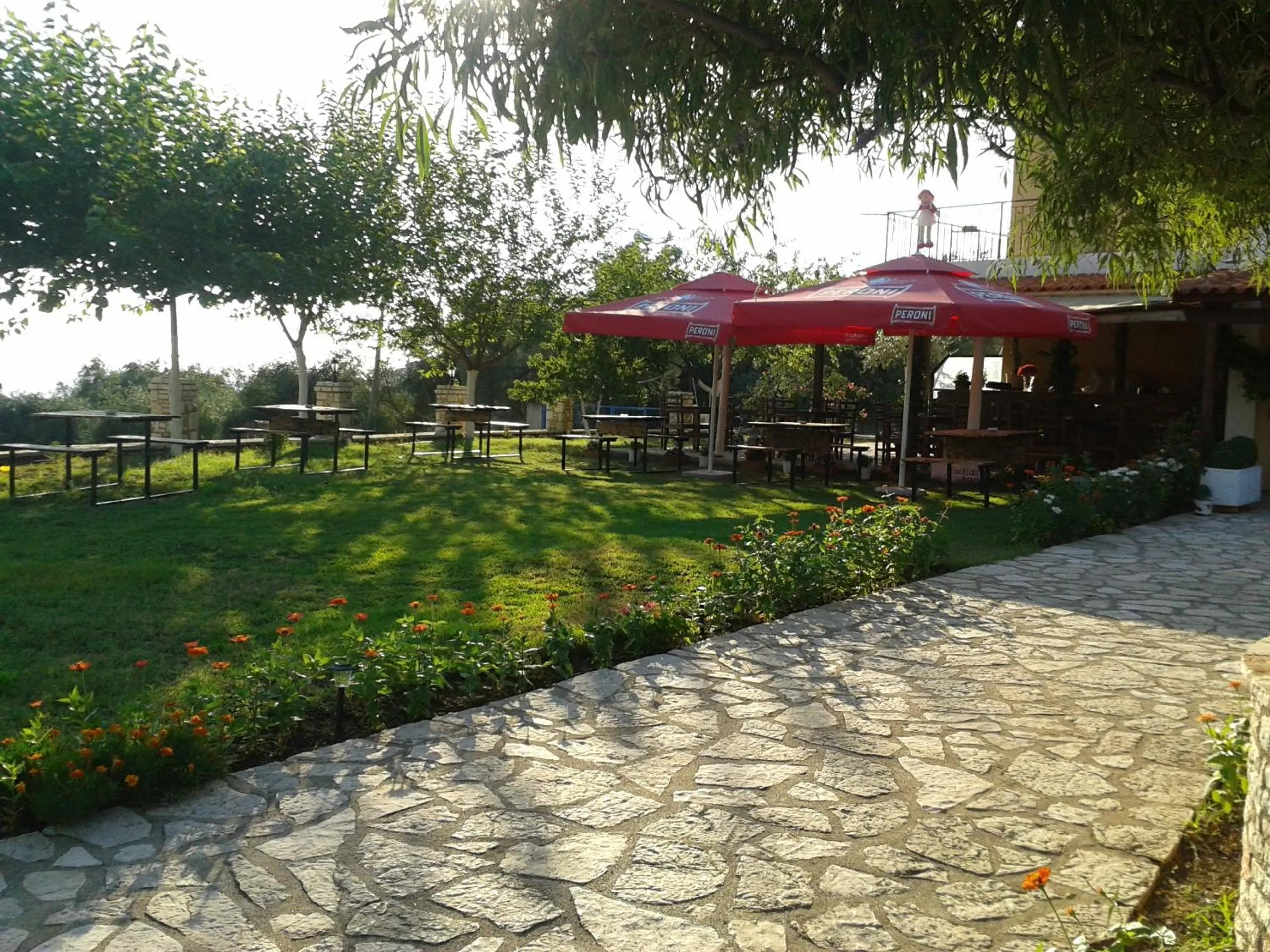 Red umbrellas over garden tables on the lawn, with a flagstone path in the foreground