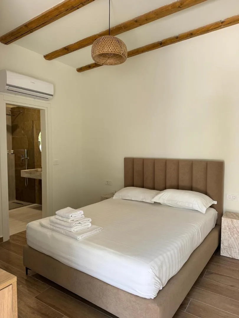 A double bed with an upholstered headboard under timber beams, the stone-tiled shower room through the door
