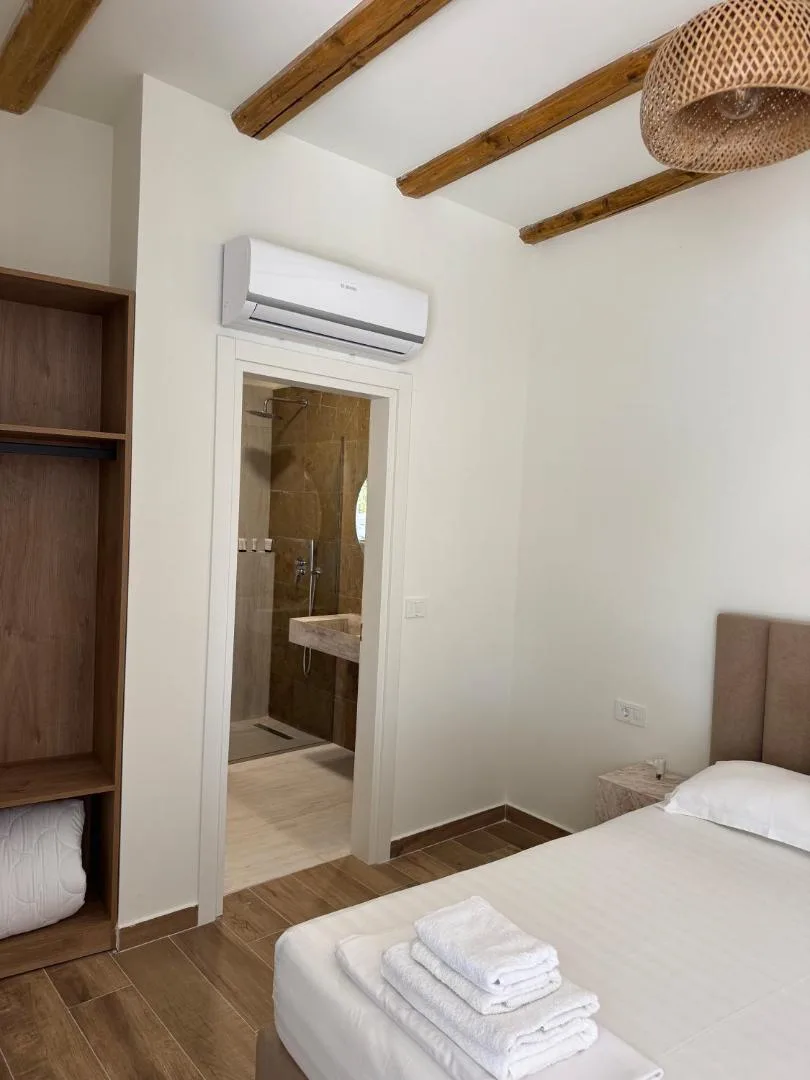 A bedroom with timber ceiling beams and a rattan pendant lamp, a double bed and a door open to the light