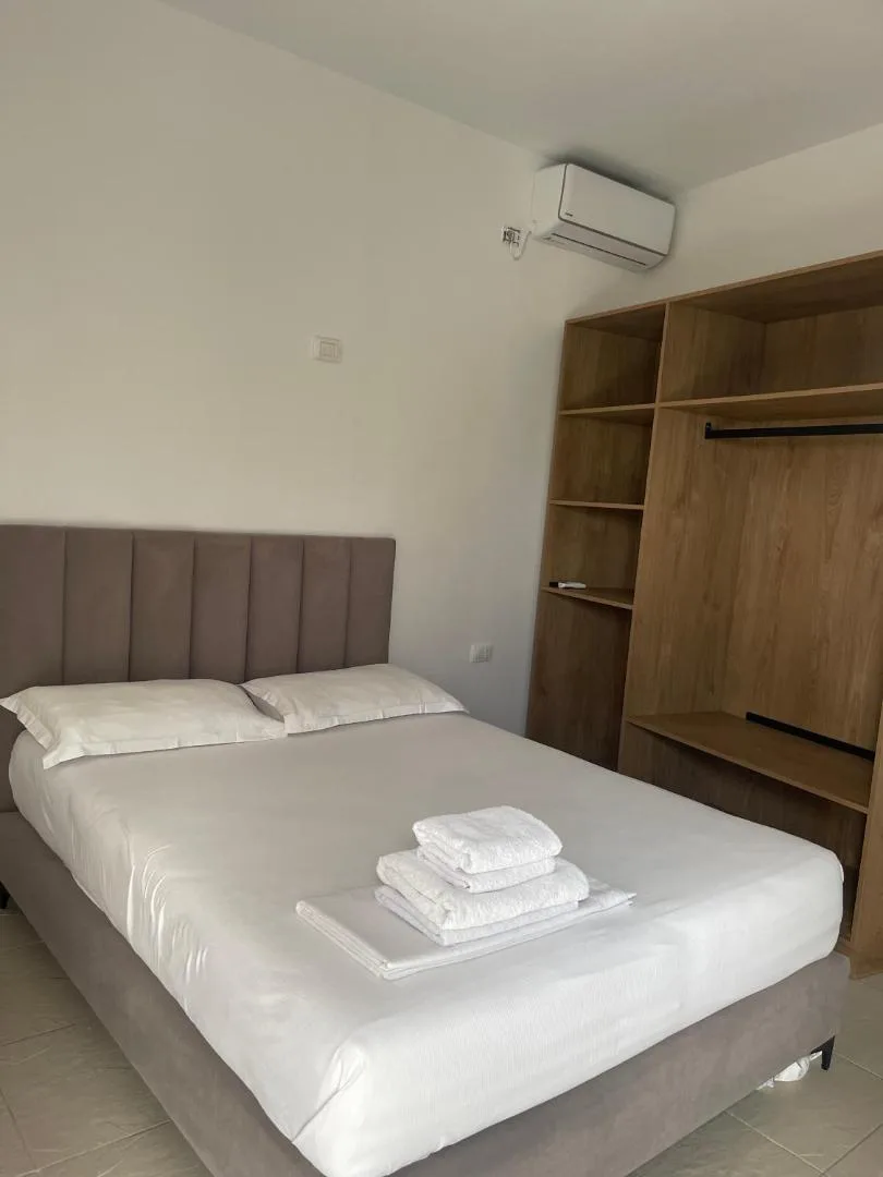 A double bedroom with an open timber wardrobe and an air-conditioning unit on the white wall