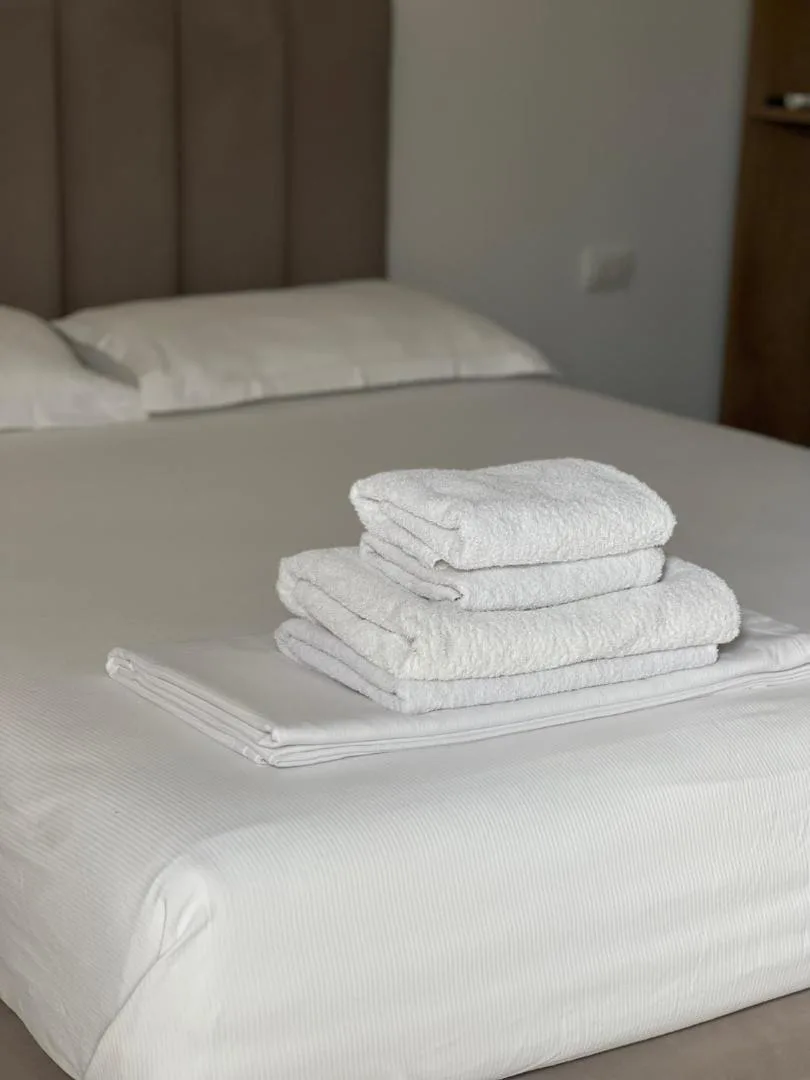 A double bed with folded towels in a white bungalow room with a grey upholstered headboard