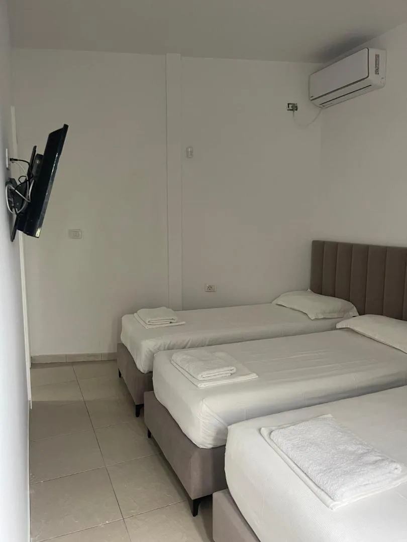 Three single beds made with white linen in a bungalow room with a wall-mounted TV