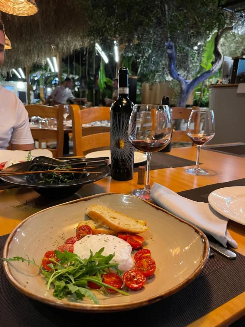 Burrata with cherry tomatoes and rocket on a stoneware plate, red wine poured, on the restaurant terrace in the evening