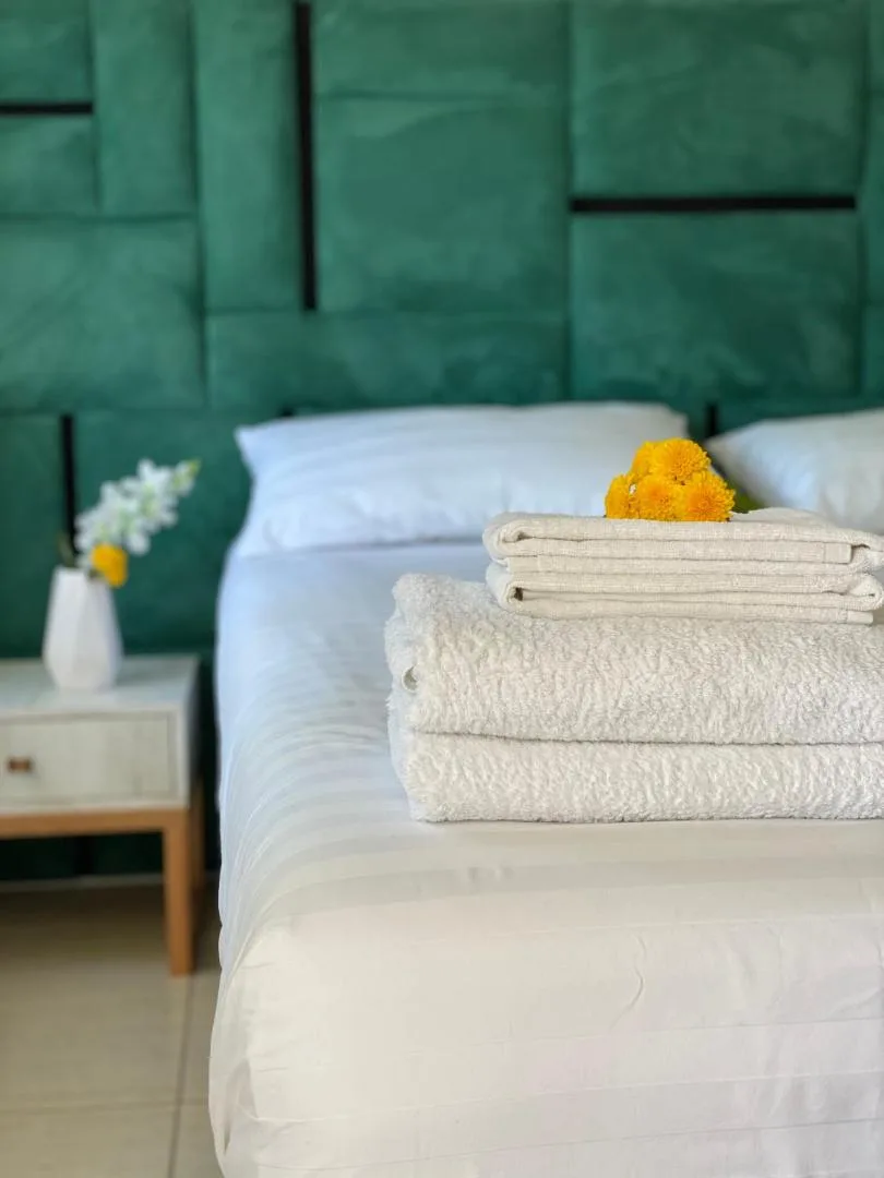 A made double bed against a deep green panelled headboard, with flowers on the bedside table