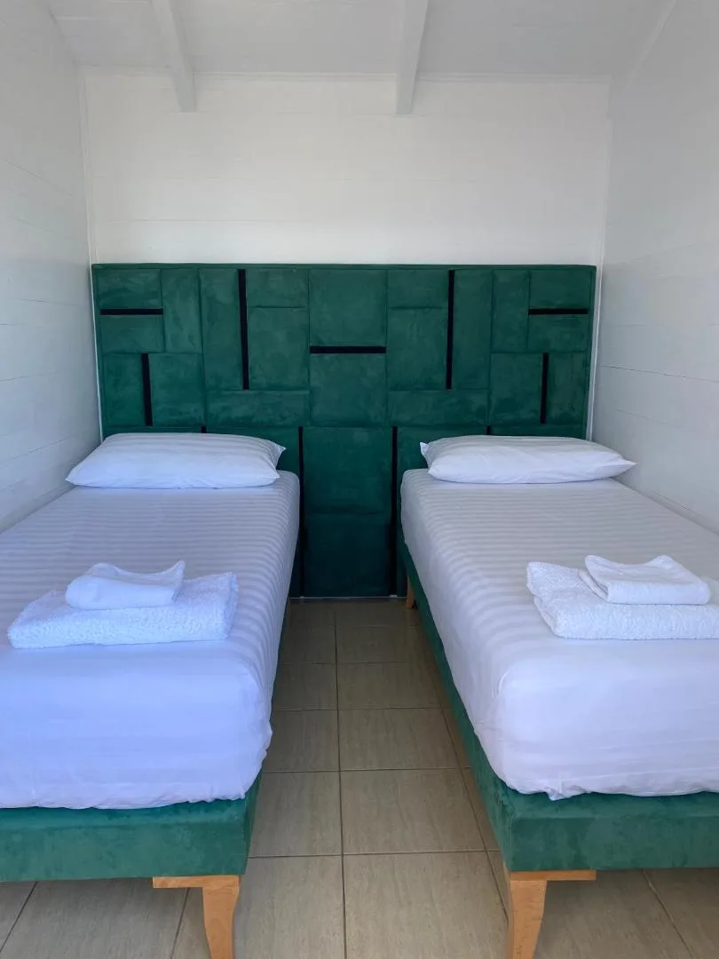 Two single beds on green bases under a deep green panelled headboard in a white timber room