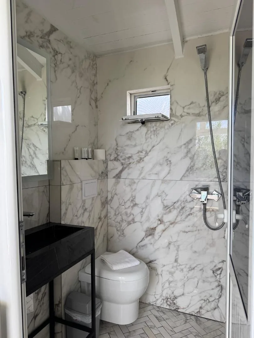 A shower room in white marble-effect tiles with a black basin stand and a glass shower