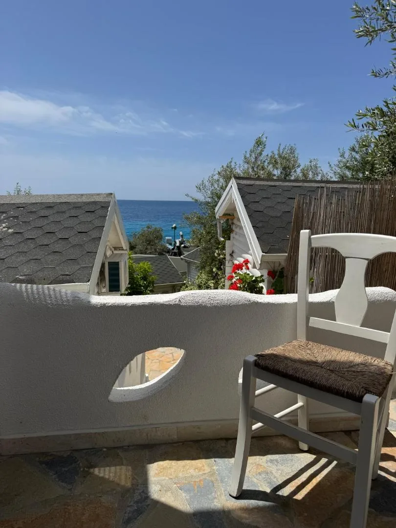 A whitewashed terrace with a rush chair, looking over the grey roofs of the bungalows to the sea