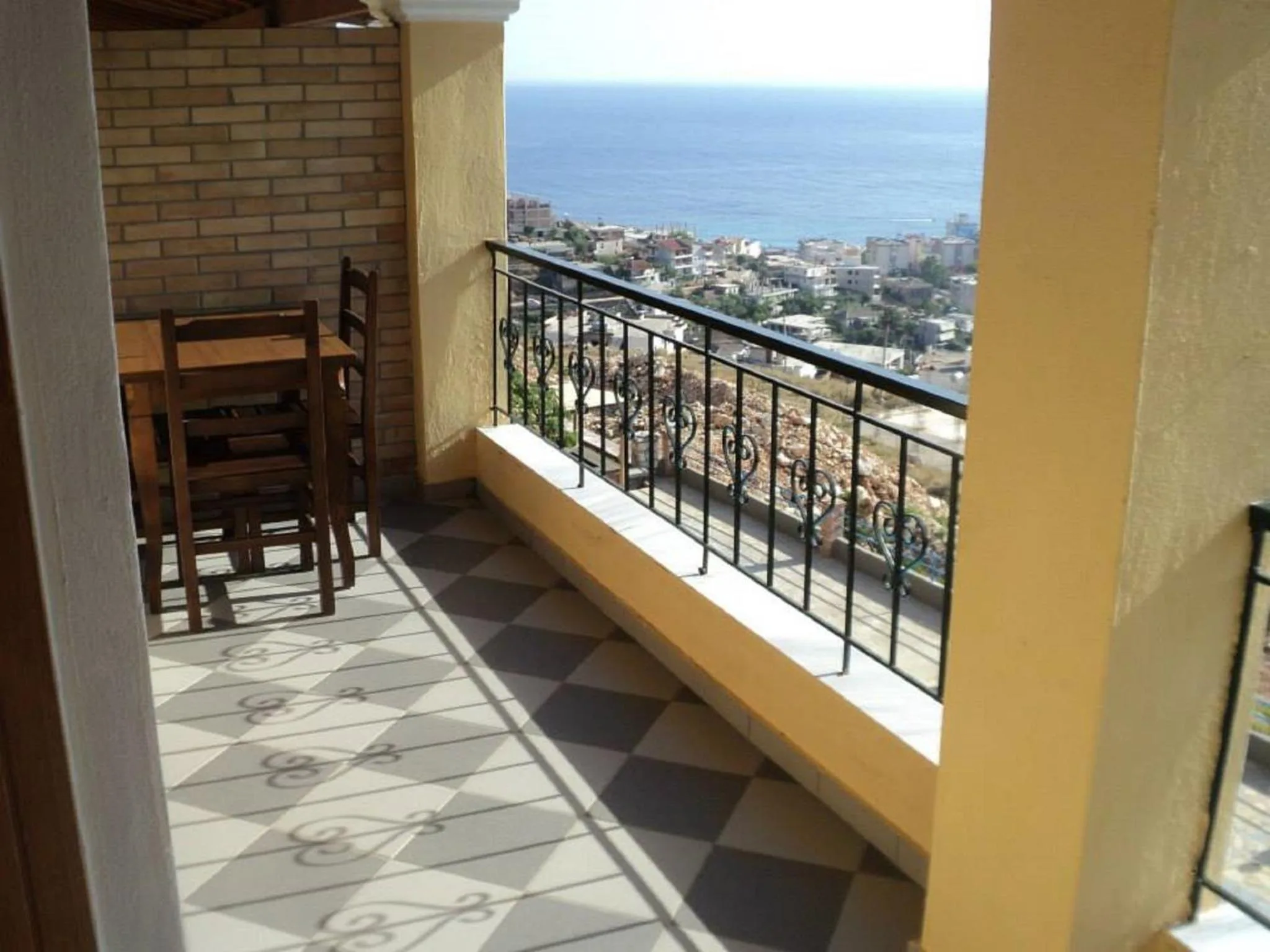 A tiled balcony with a wooden table and chairs, the town and the sea below the railing