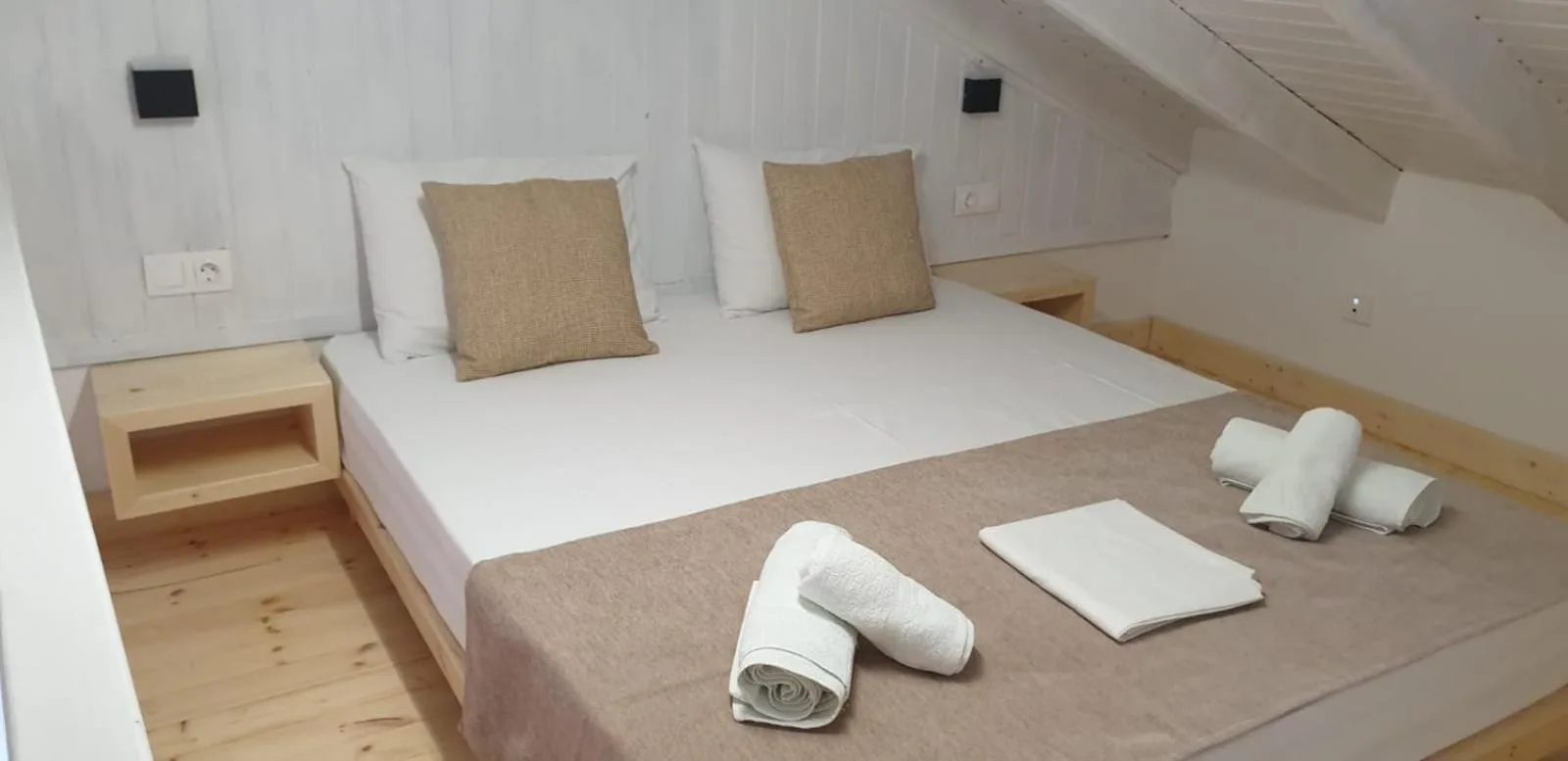A double bed with two cushions and folded towels on a pine floor