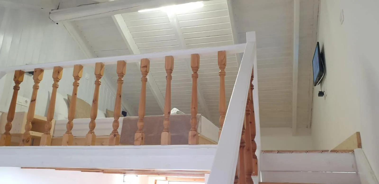 The sleeping loft behind a turned pine balustrade under a white boarded ceiling