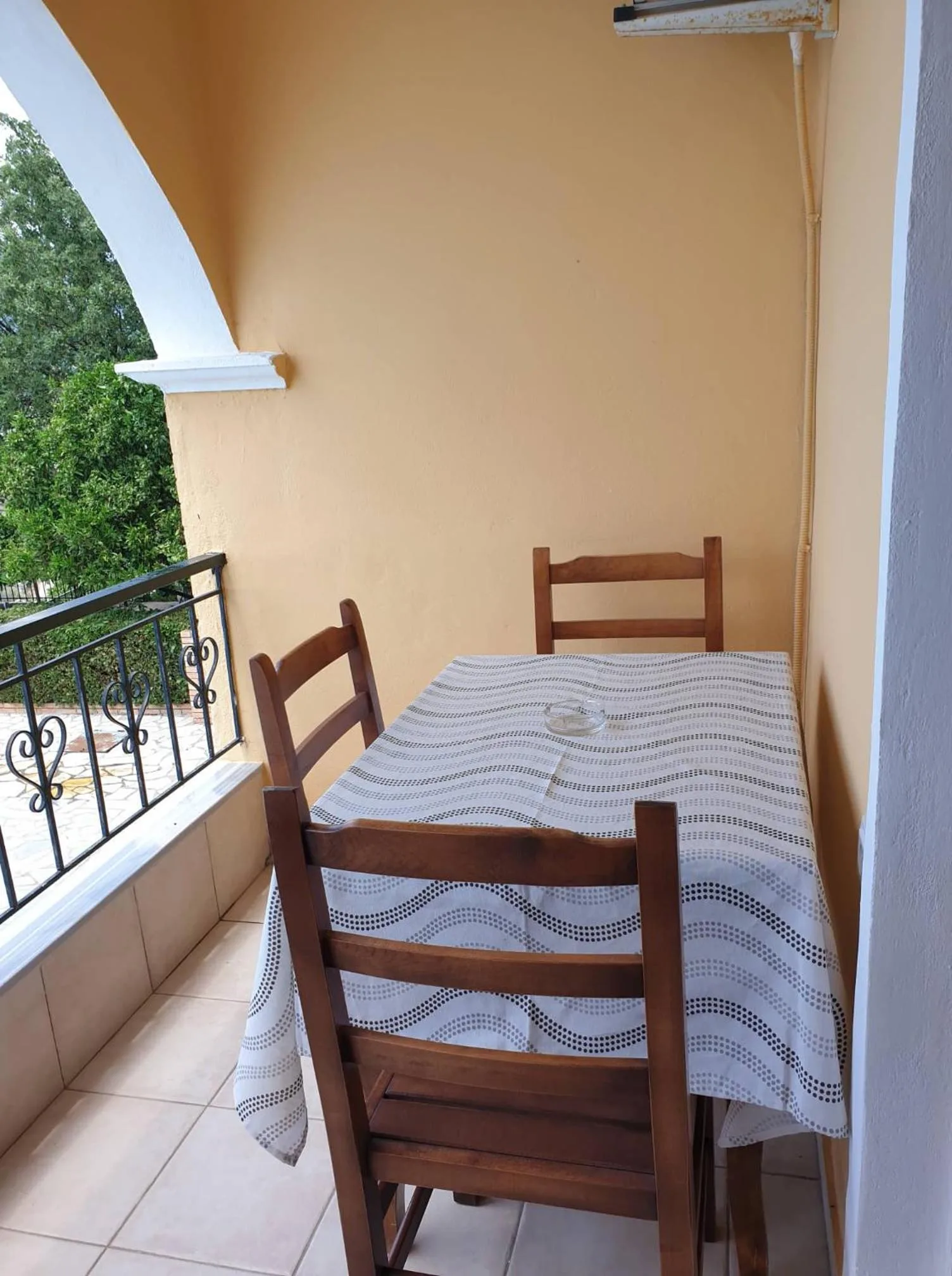 A balcony under an arch with a table and two chairs and a view of trees