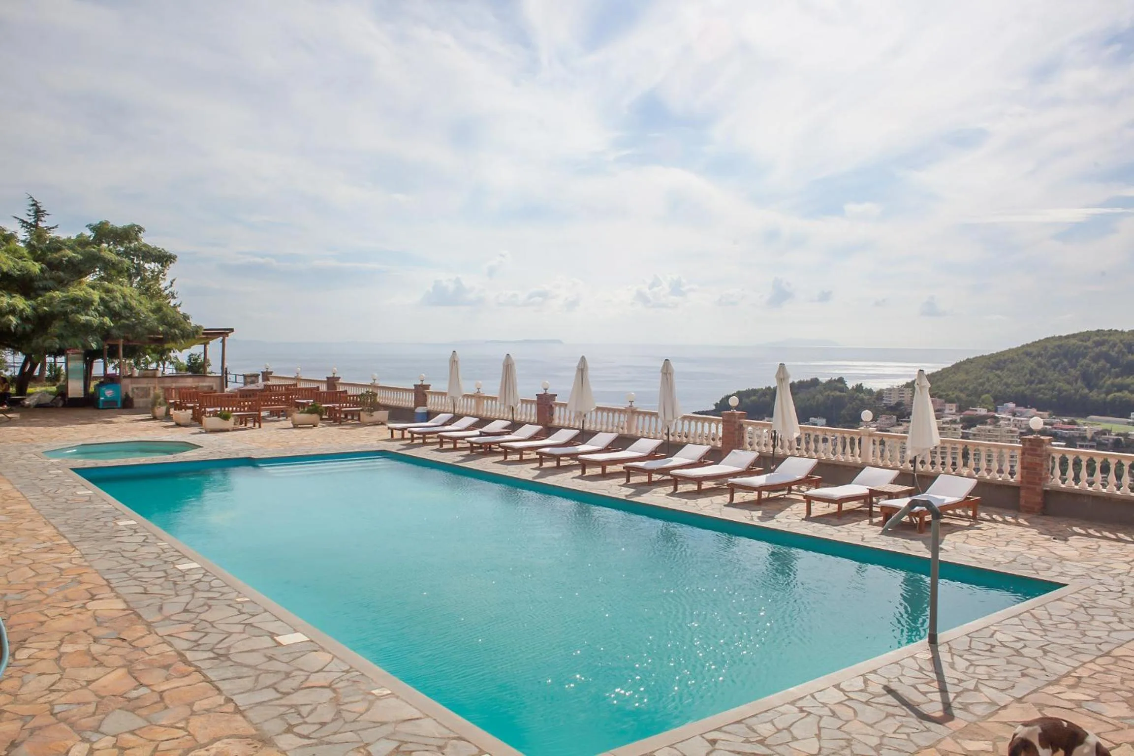 The pool on its flagstone deck with loungers and umbrellas along the rail and the sea on the horizon