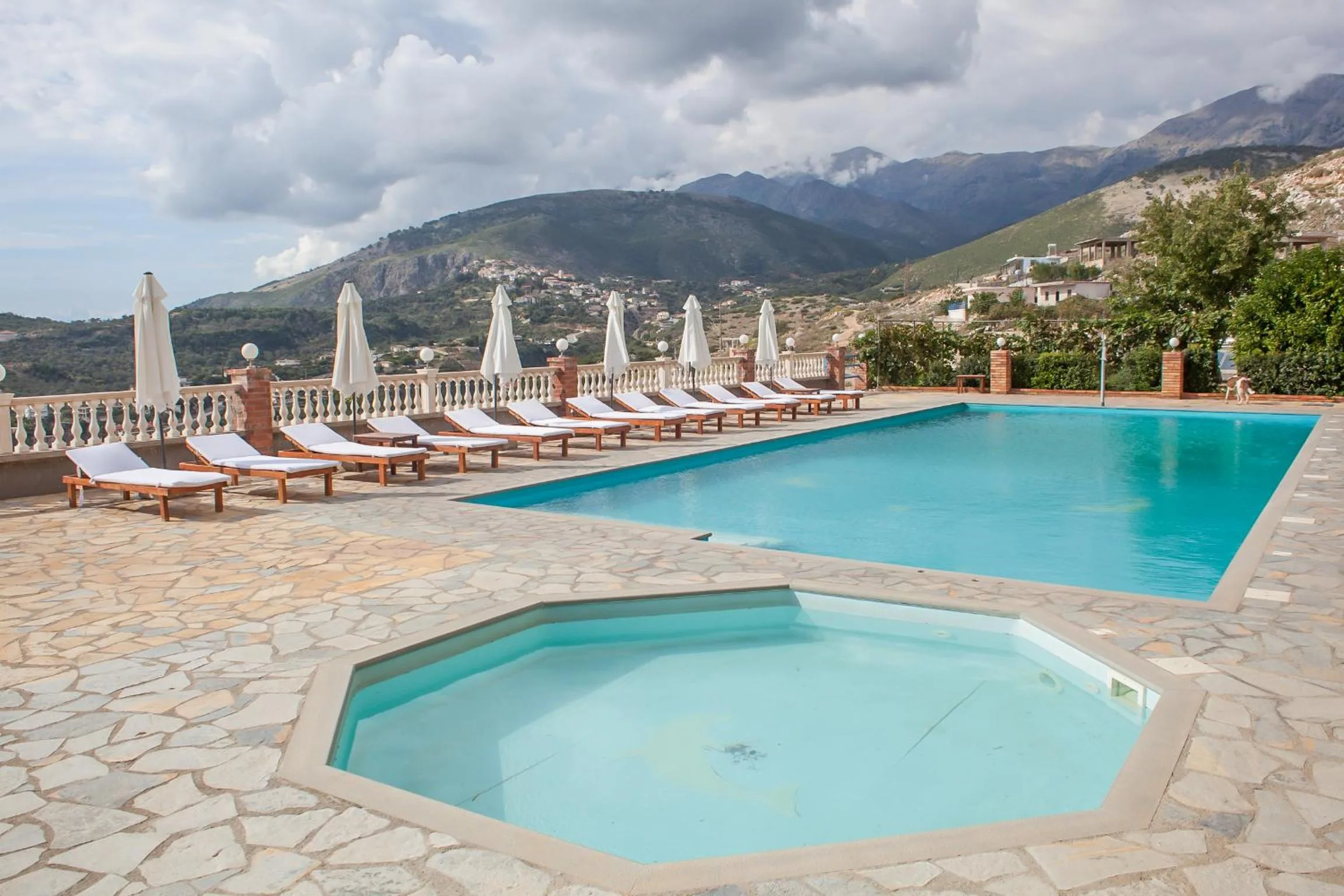 An octagonal paddling pool in front of the main pool on a flagstone deck, mountains behind