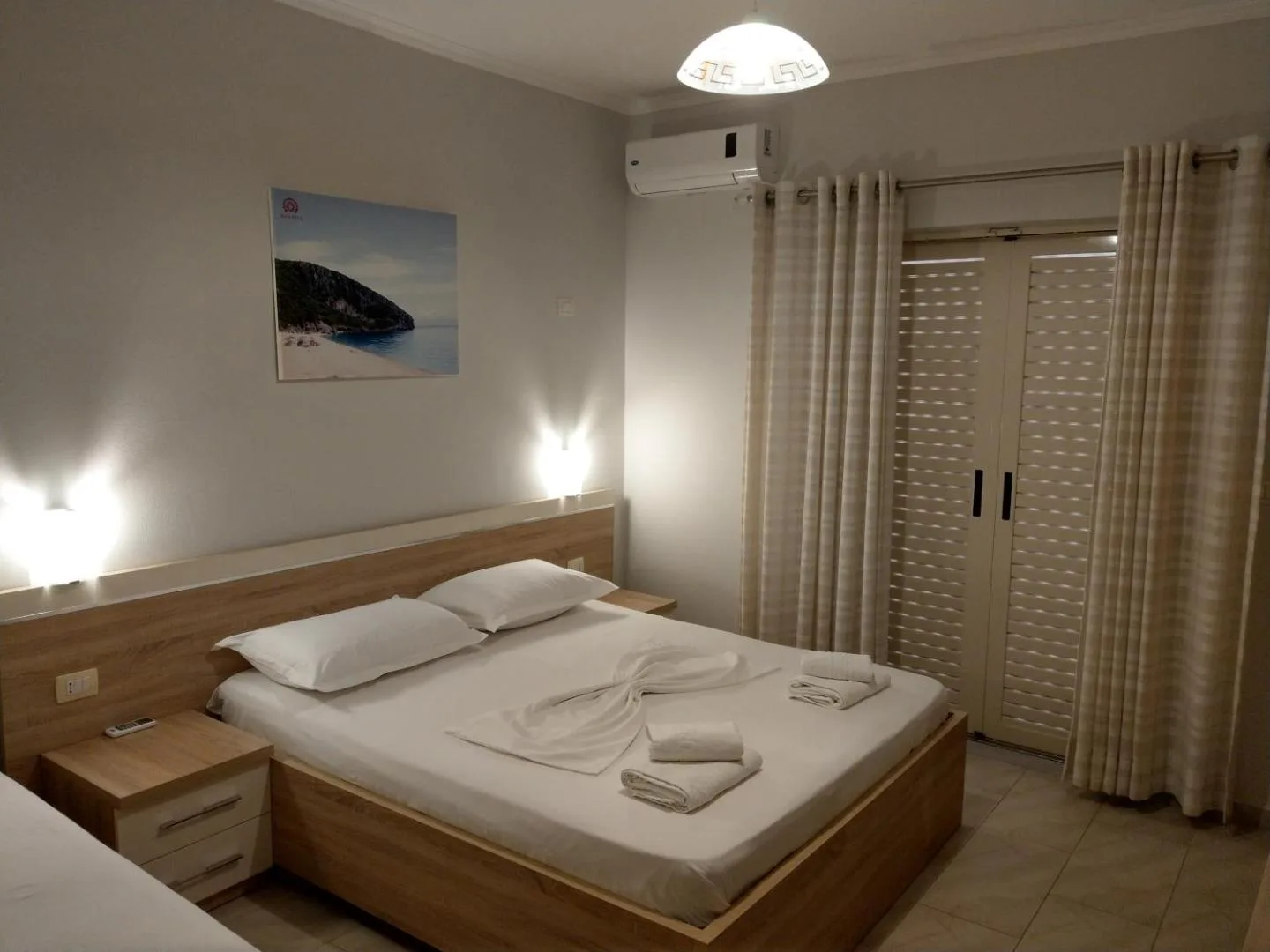 A double room at Augustus Hotel with a light oak bed made in white, bedside lamps, a sea photograph on the wall and long curtains over the terrace doors