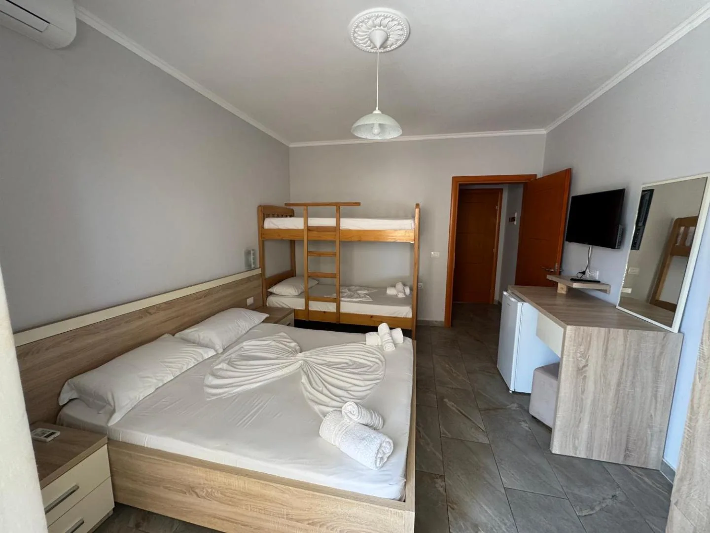 A family room at Augustus Hotel with a double bed and a wooden bunk bed, a desk, a wall-mounted television and a tiled floor