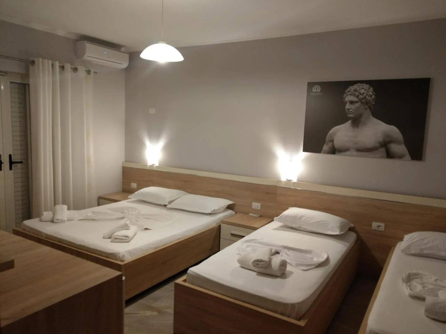 A room at Augustus Hotel with a double bed and two singles in light oak, under a large print of a classical marble statue