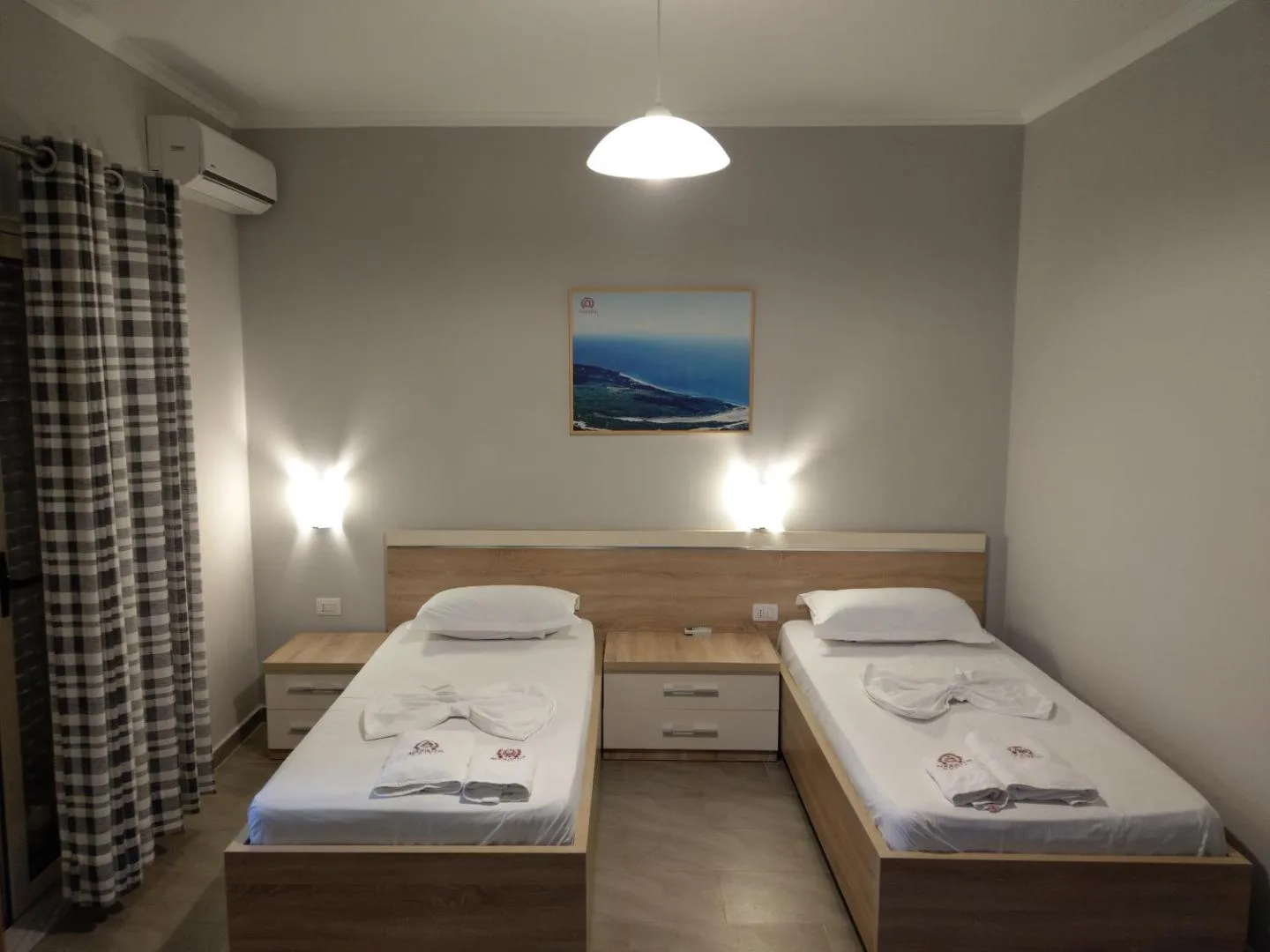 A twin room at Augustus Hotel with two single beds made in white either side of a bedside table, under a framed photograph of the sea