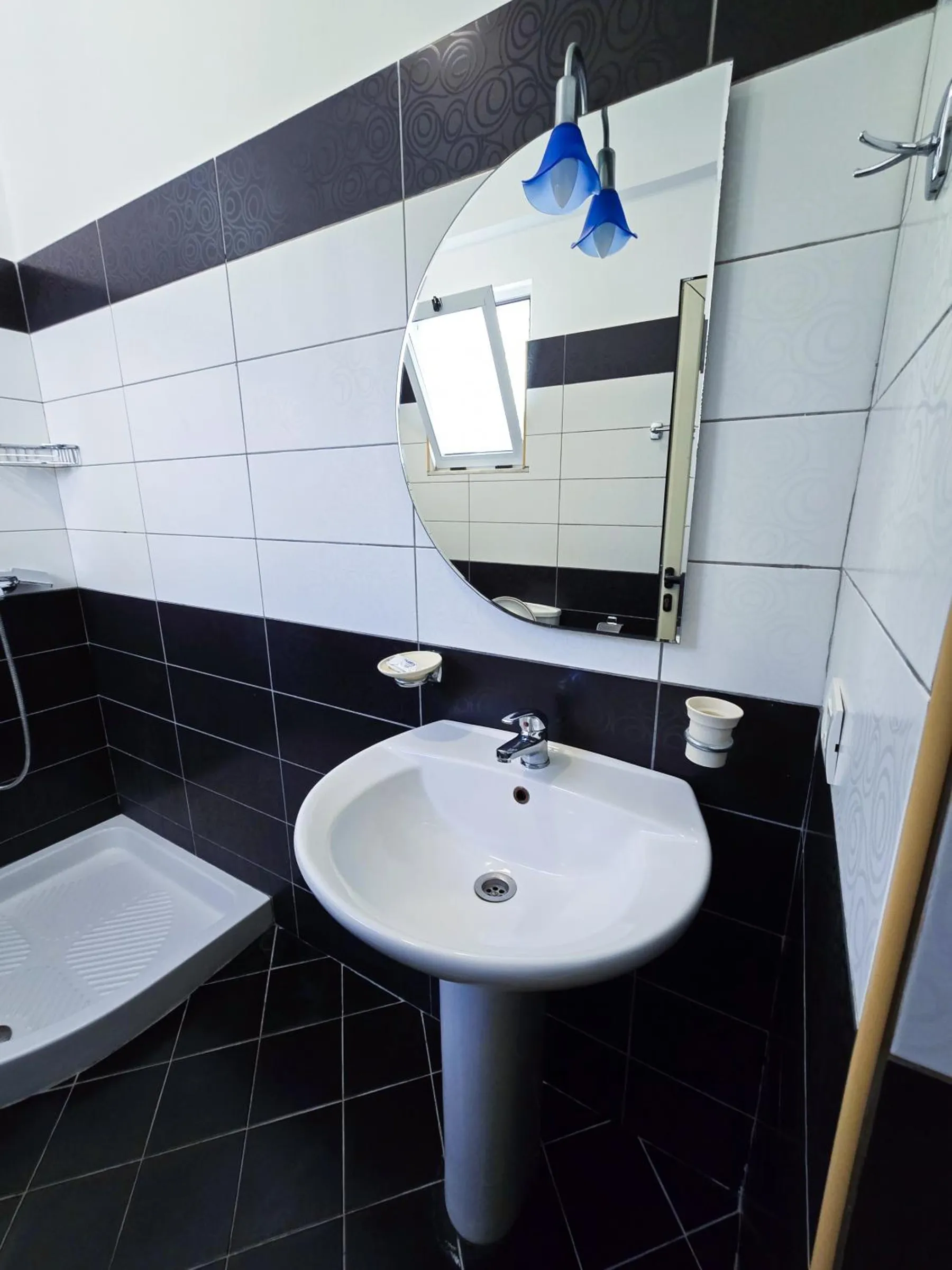 A bathroom tiled white above and black below, with a pedestal basin, an oval mirror and a shower tray