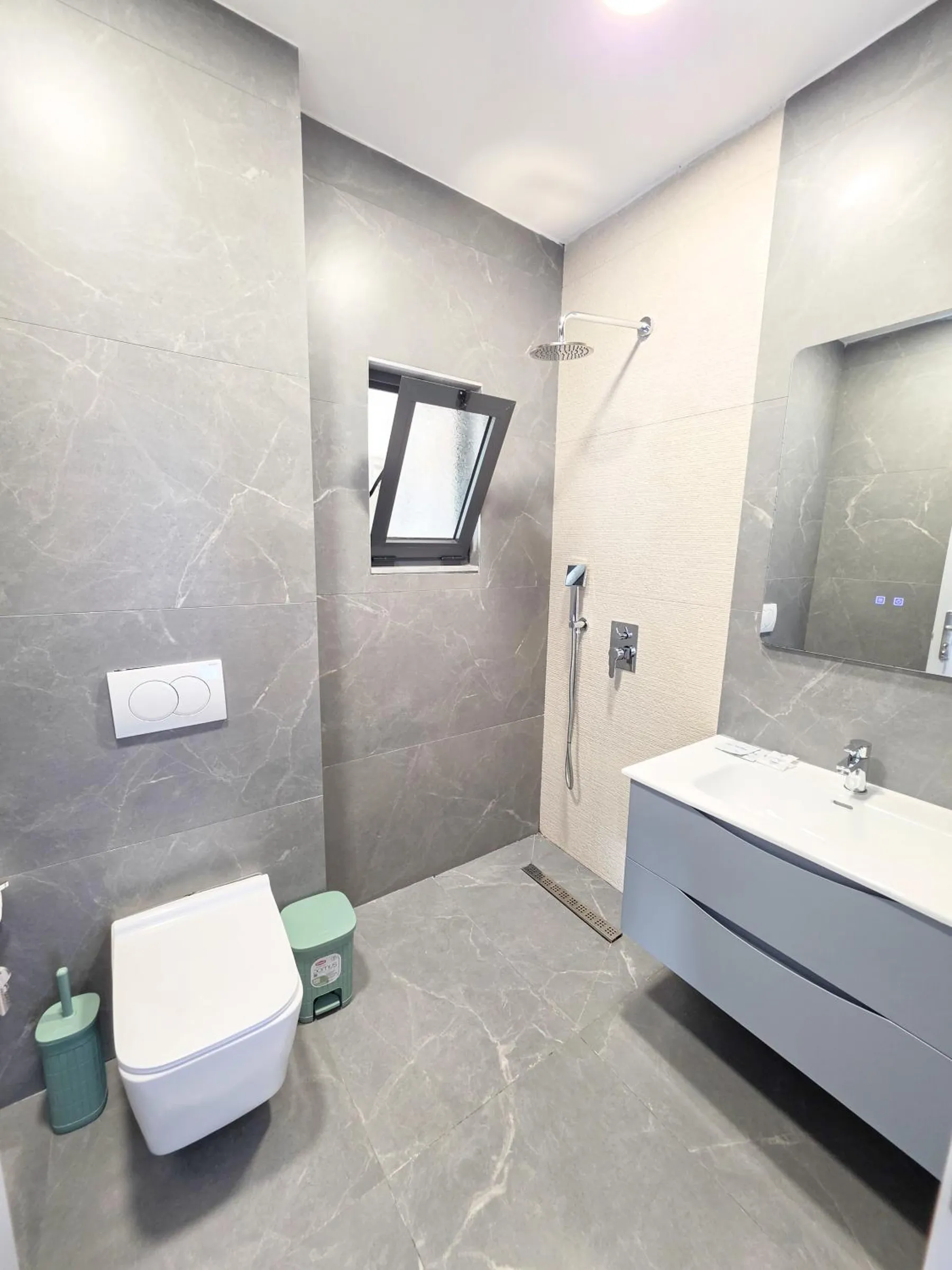 A walk-in shower room in grey stone-effect tile with a wall-hung toilet, a floating grey vanity and a frosted window