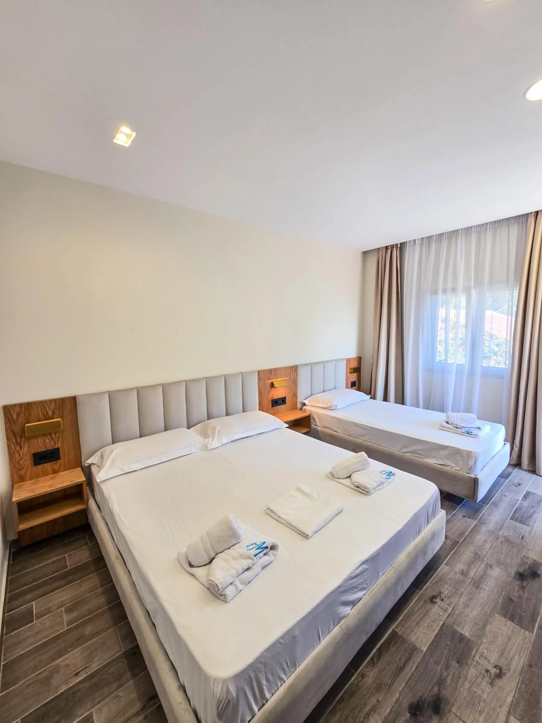 A double bed and a single bed with matching grey upholstered headboards and oak bedside panels on a wood-effect floor