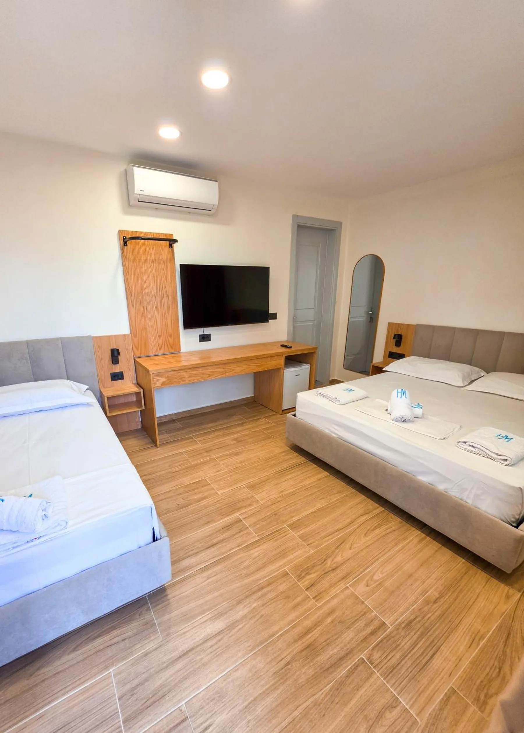A room with a double bed and a single bed, an oak desk with a television above it and an air conditioner on the wall