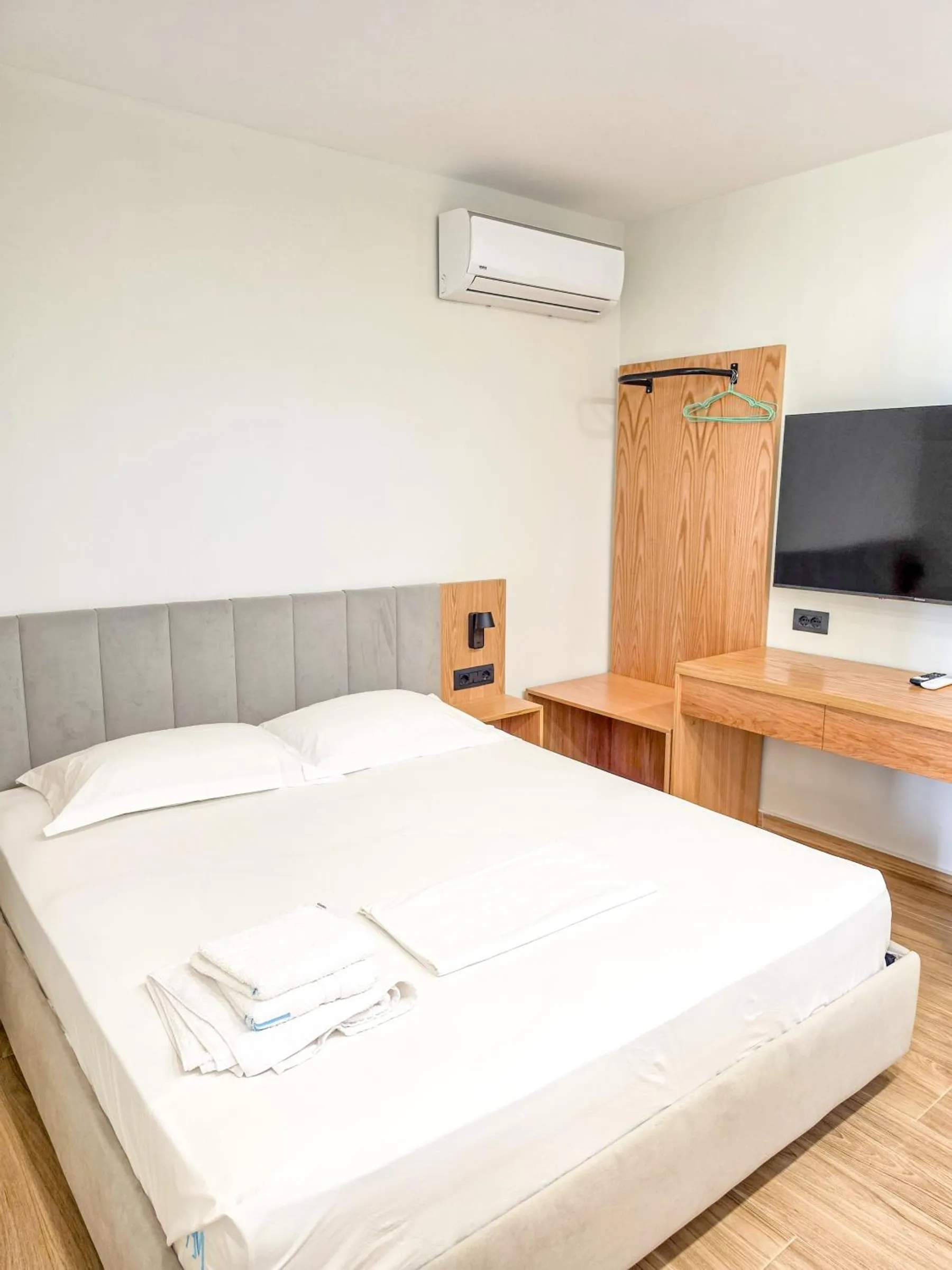 A double bed with a grey upholstered headboard, an oak desk, a wall-mounted television and an oak coat stand
