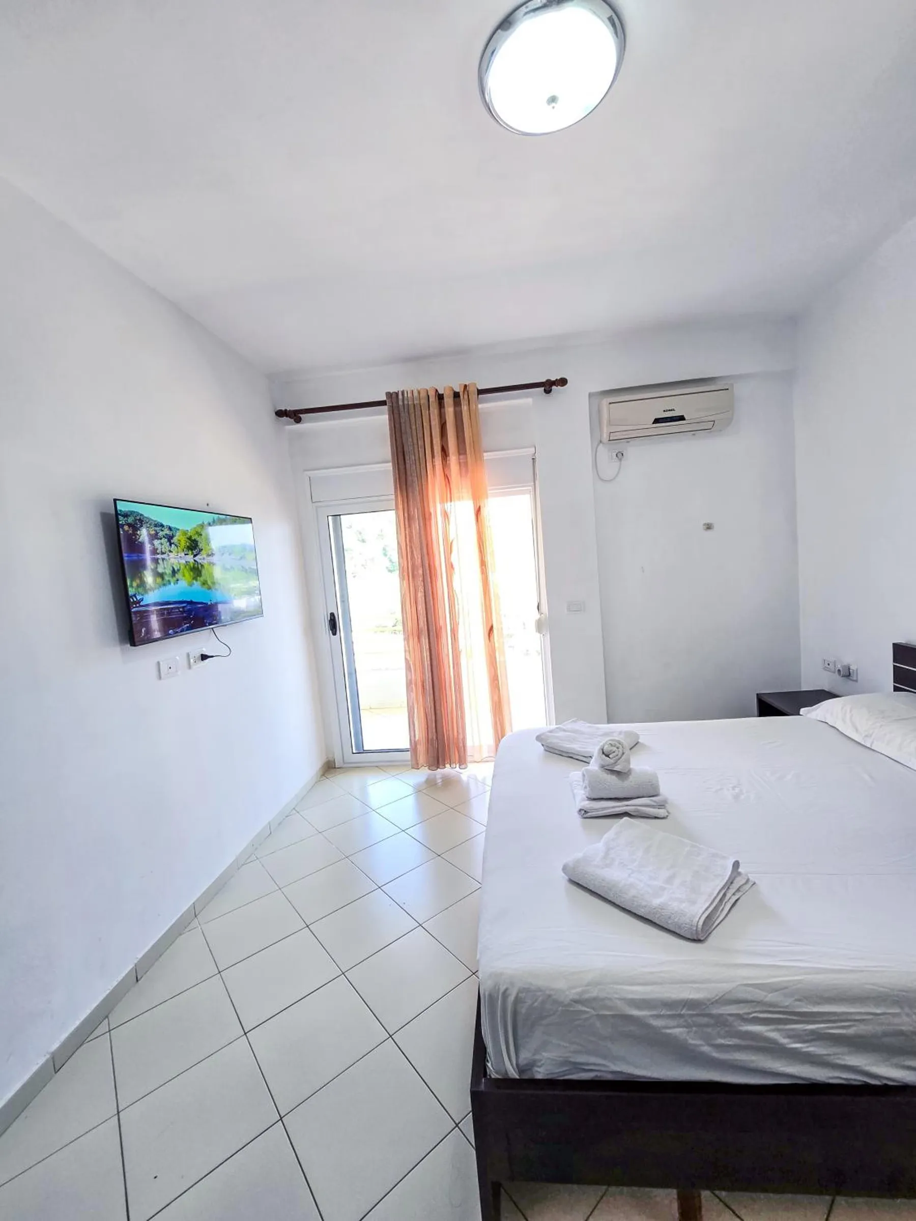 A white room with a tiled floor, a double bed with a dark frame and a glazed door to the balcony at the far end