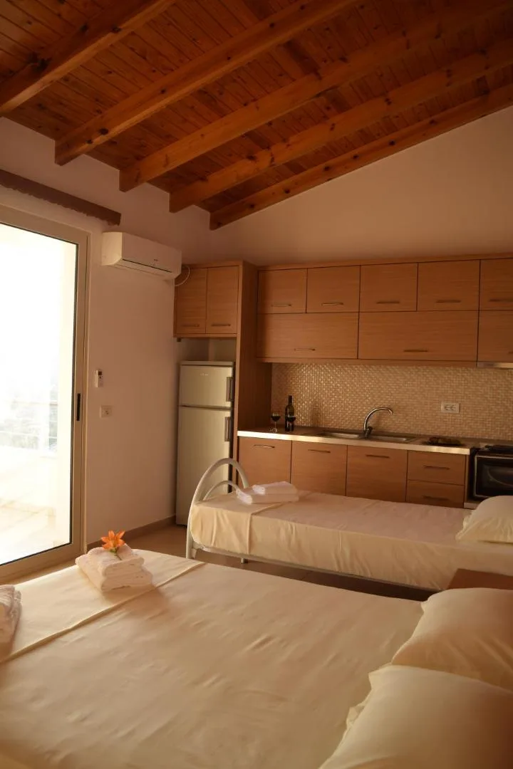 A fitted kitchen of pale wood units with a worktop, sink and oven, a bed in the same room and an air conditioner above