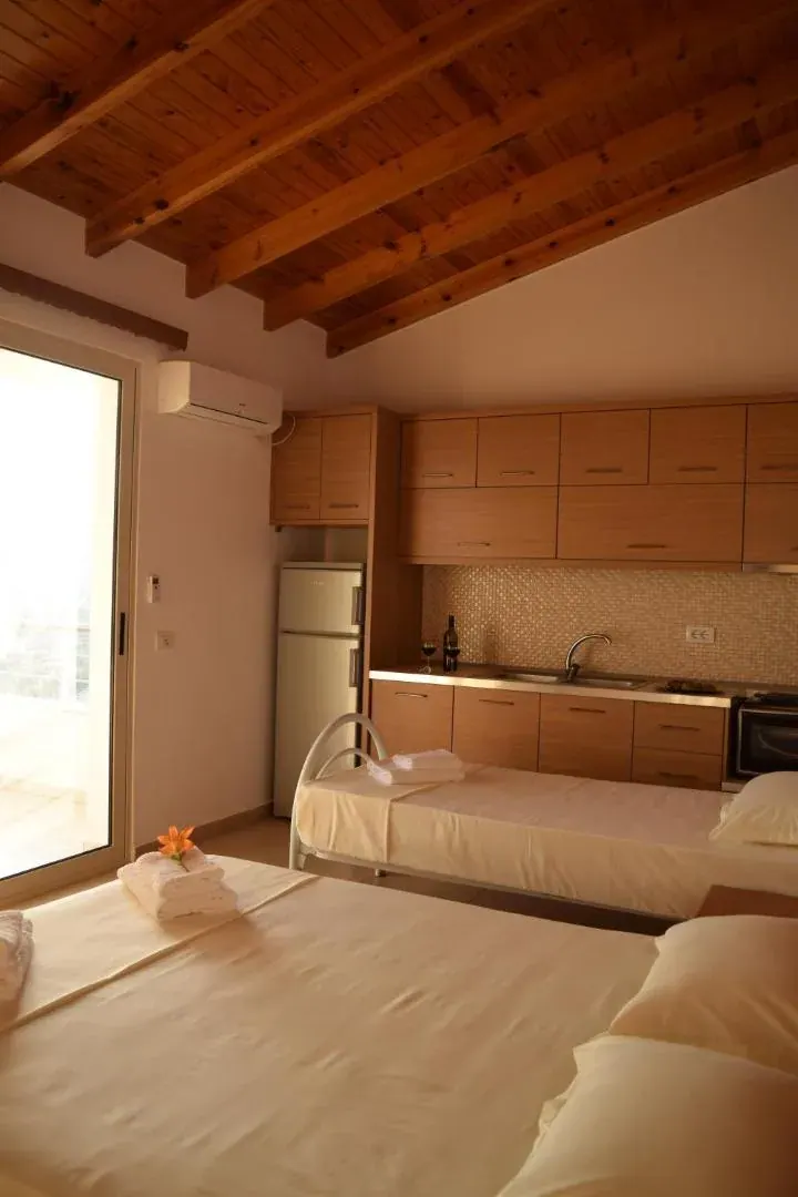 A fitted kitchen of pale wood units with a worktop, sink and oven, a bed in the same room and an air conditioner above