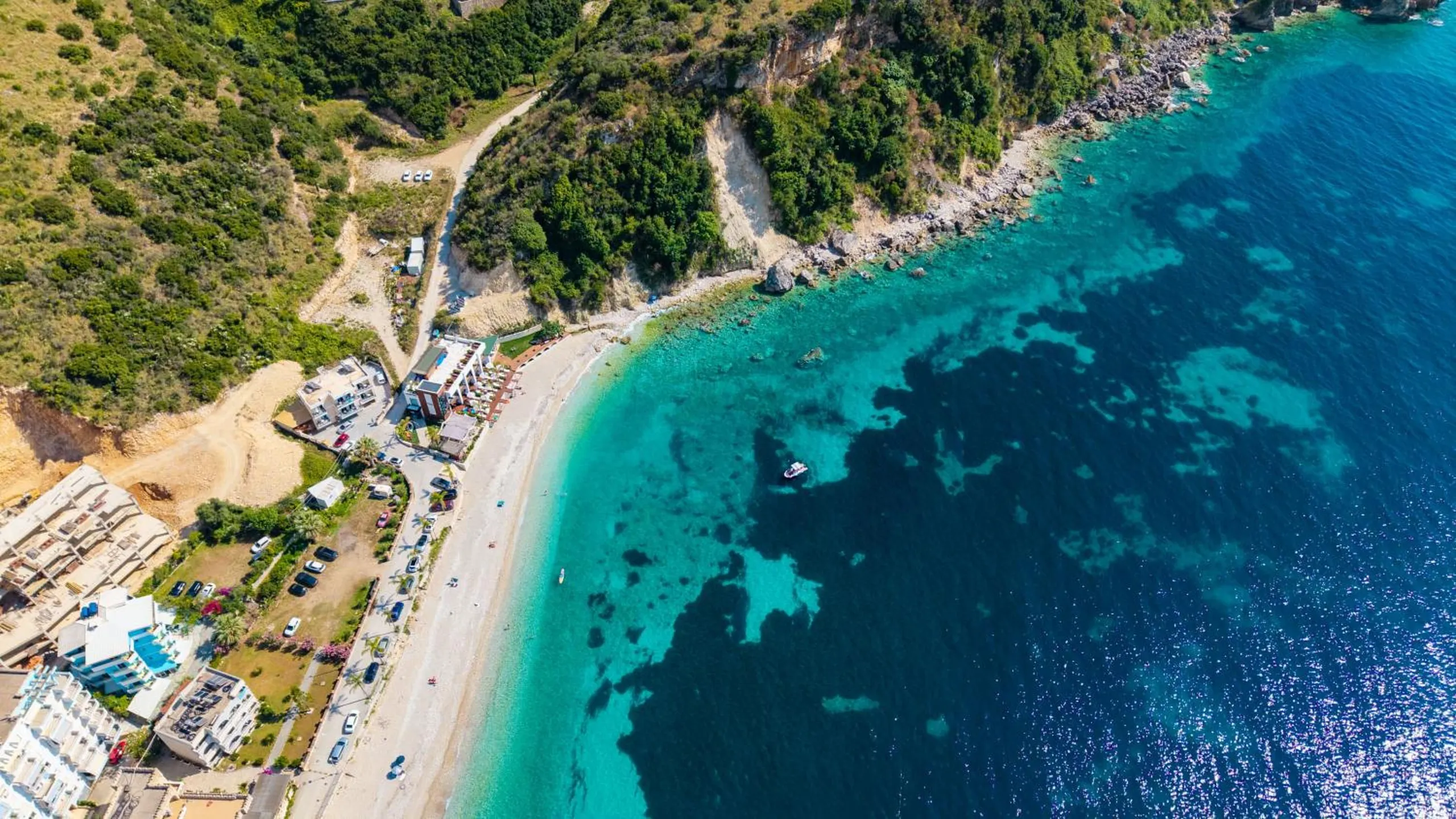 A high aerial of the south end of Potam: wooded headland, a long beach and water shading from turquoise to deep blue over the reef
