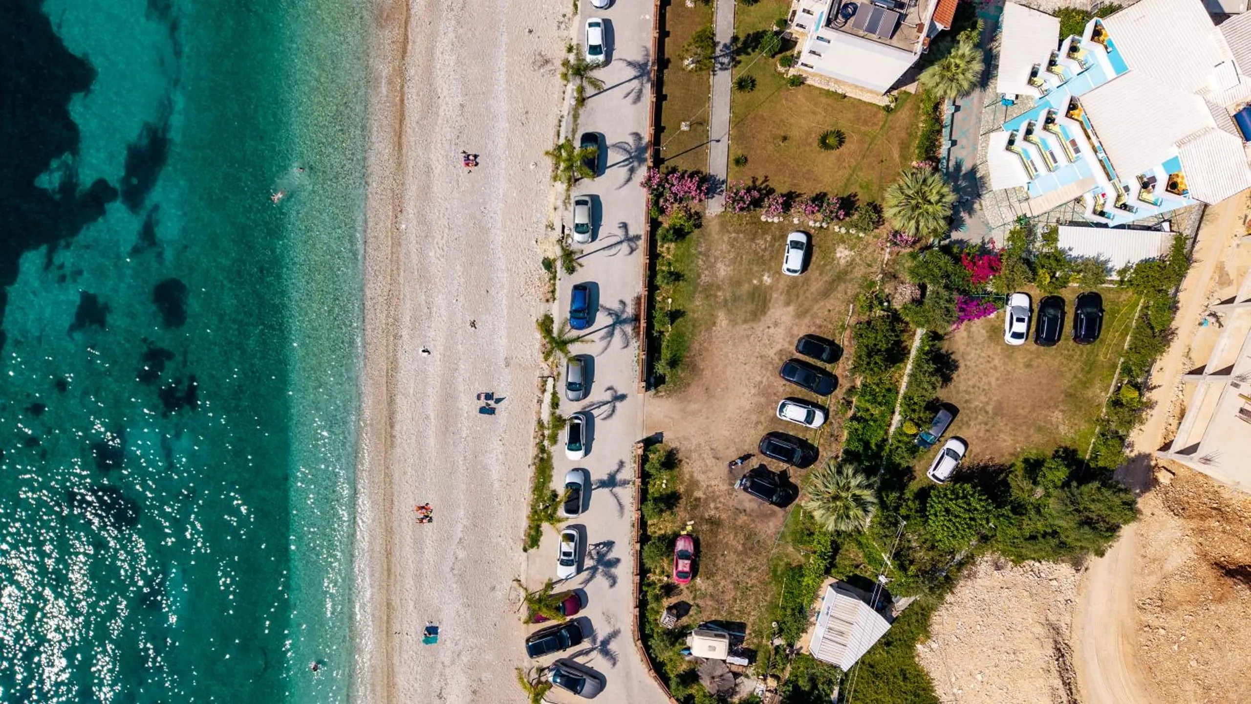 Straight down from above: turquoise water, a pale strip of beach, a promenade lined with palms and the hotel's garden and car park behind it