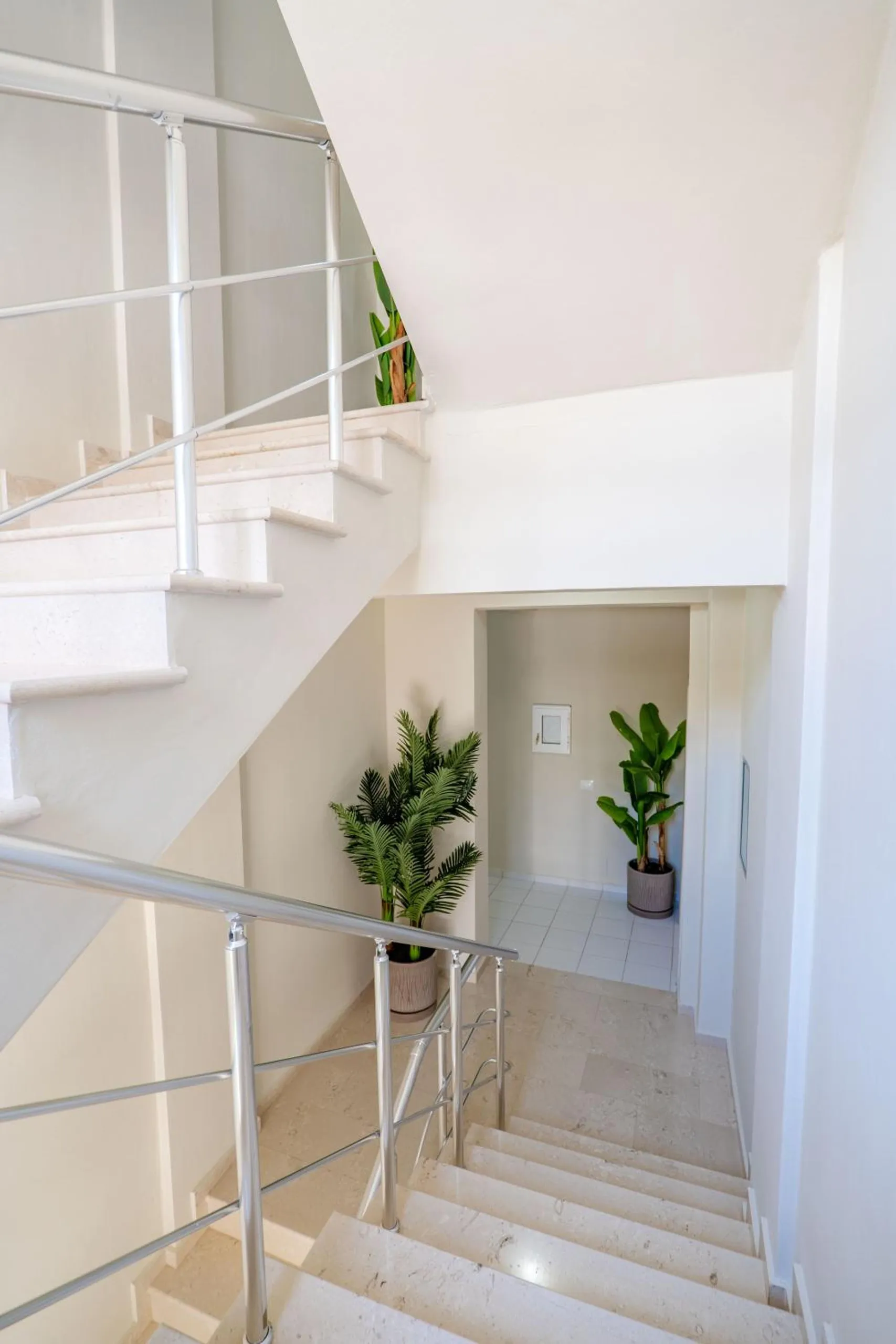A white stairwell with tiled steps and a steel handrail, a potted plant on each landing