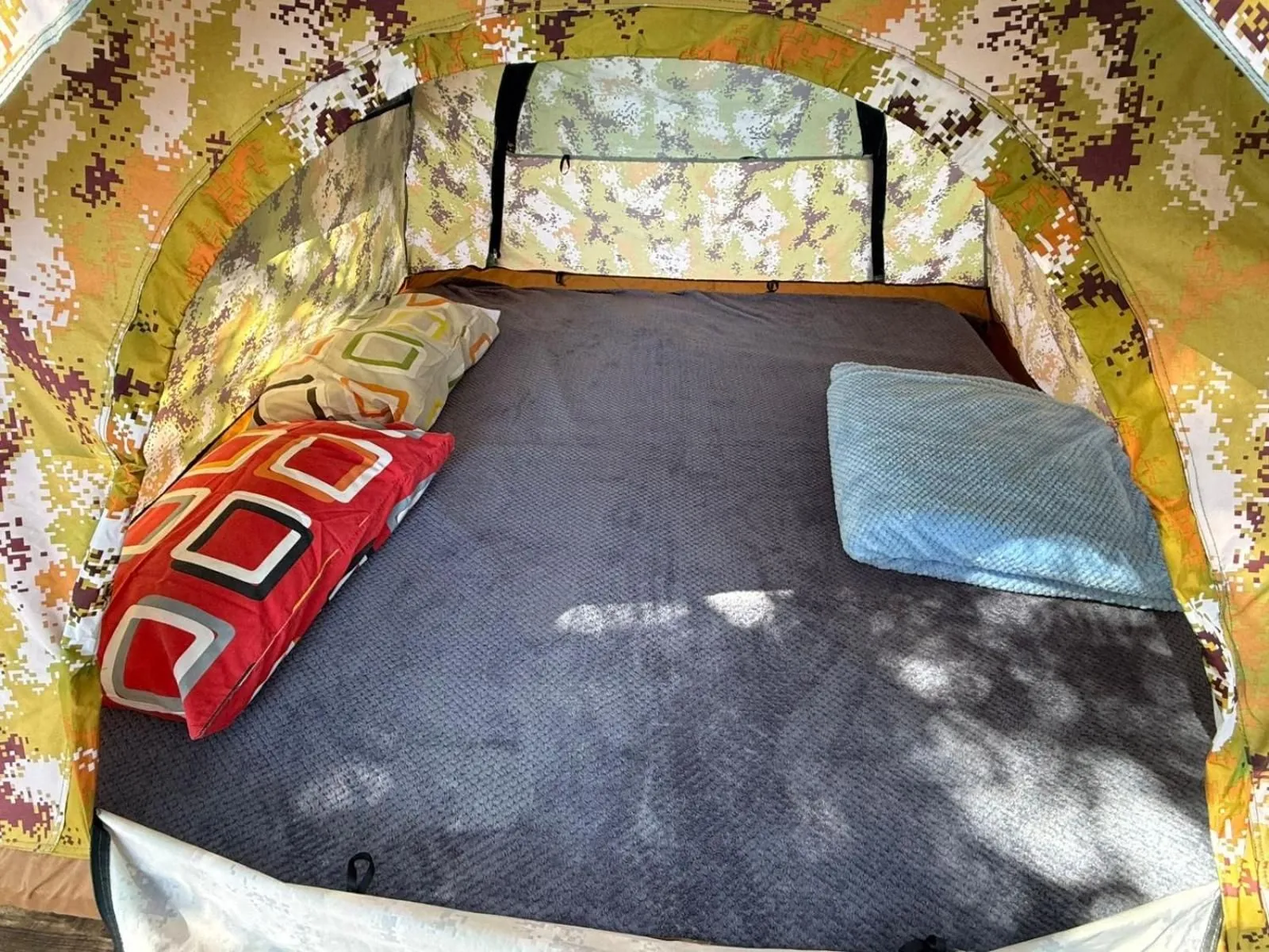 Inside a camouflage-print tent: a mattress laid with pillows and the morning light on the canvas