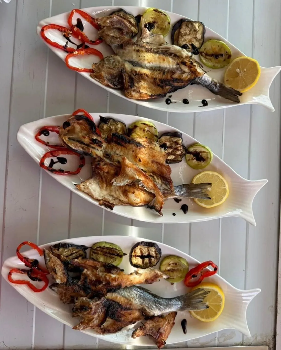 Three platters of grilled fish with lemon and grilled peppers
