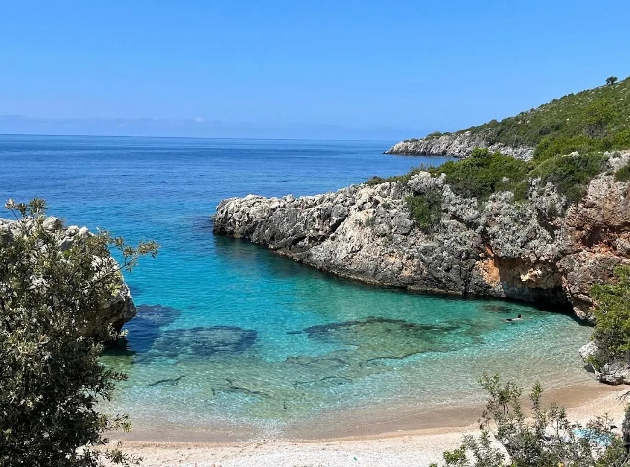 The cove at midday: clear turquoise water over pebbles below a limestone headland
