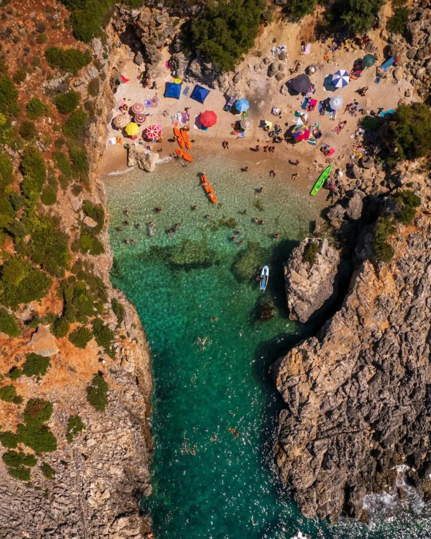 Looking straight down on the narrow inlet: green water between two rock walls, the beach and its umbrellas at the head