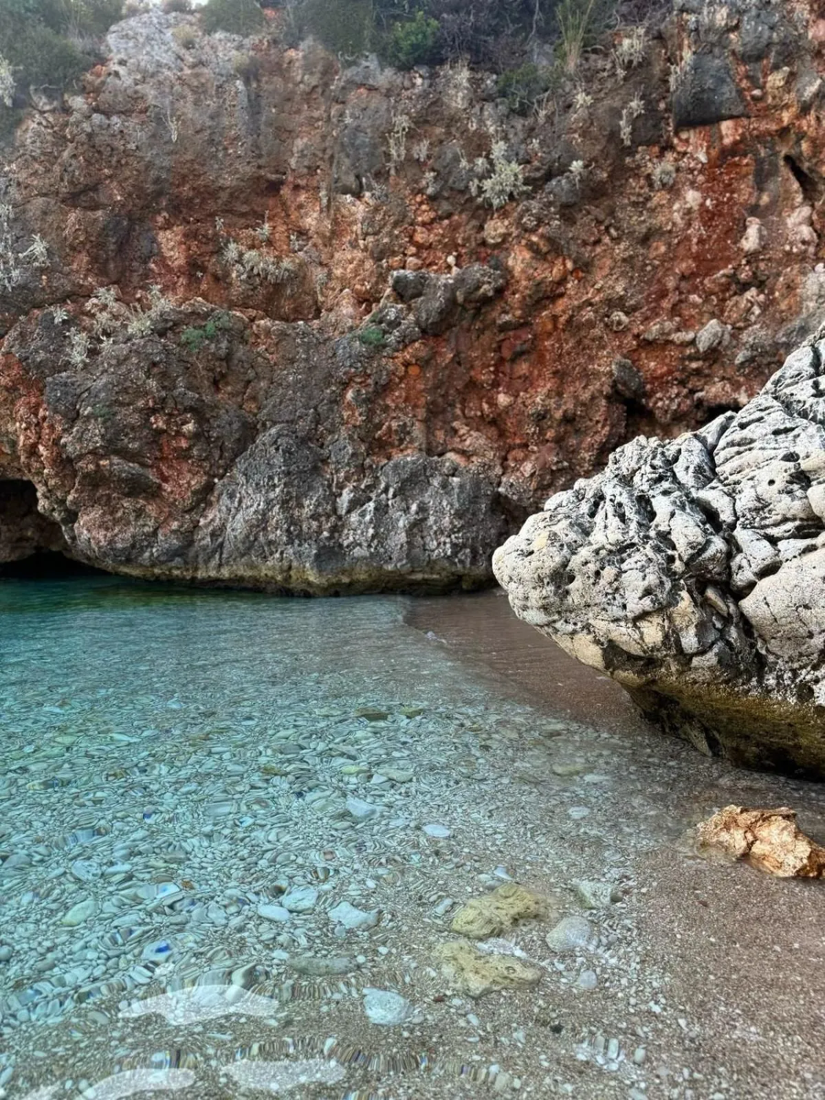 Clear shallow water over pebbles under a red limestone overhang