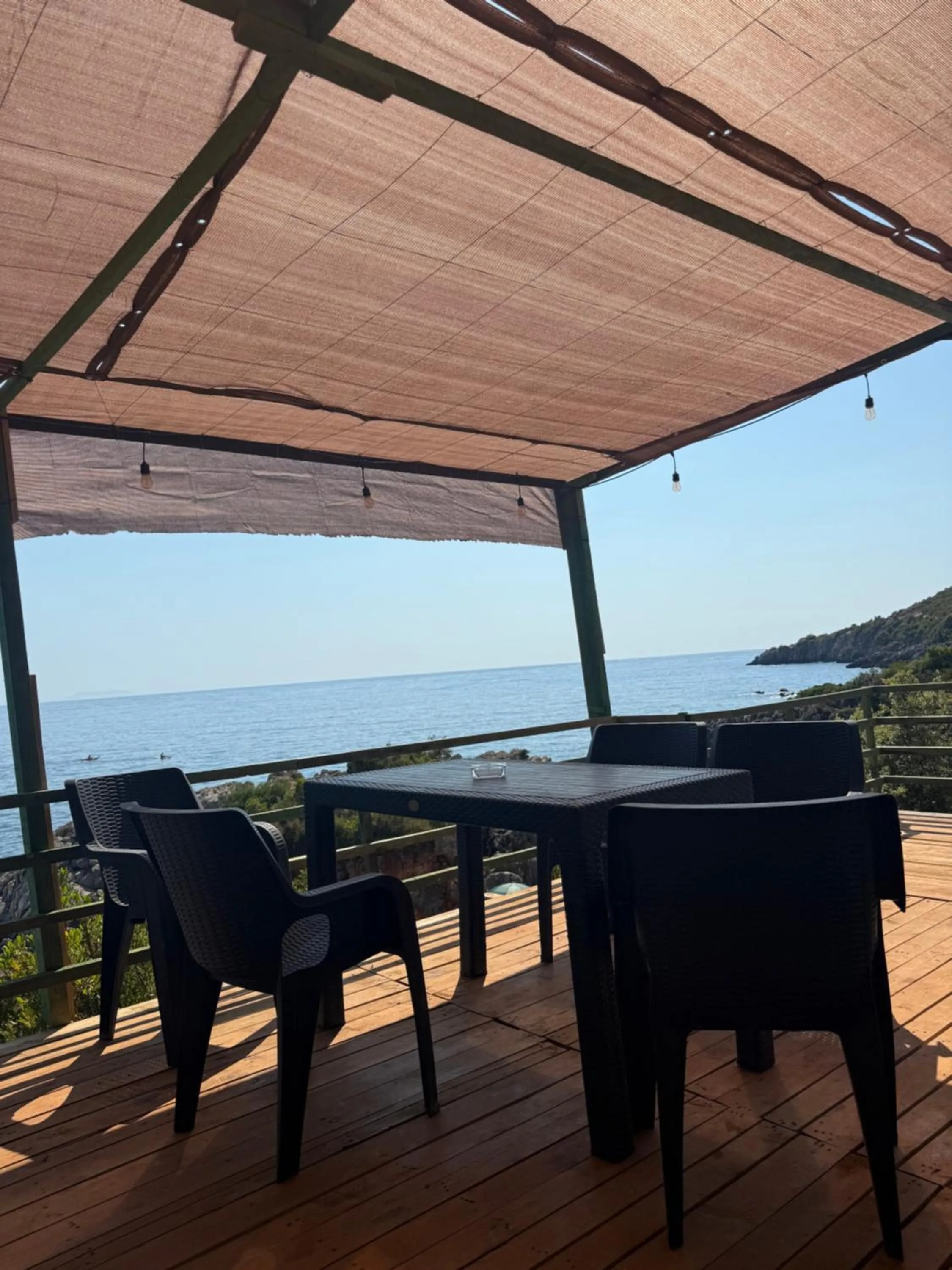The bar's plank terrace under a shade sail, tables at the rail and the sea beyond