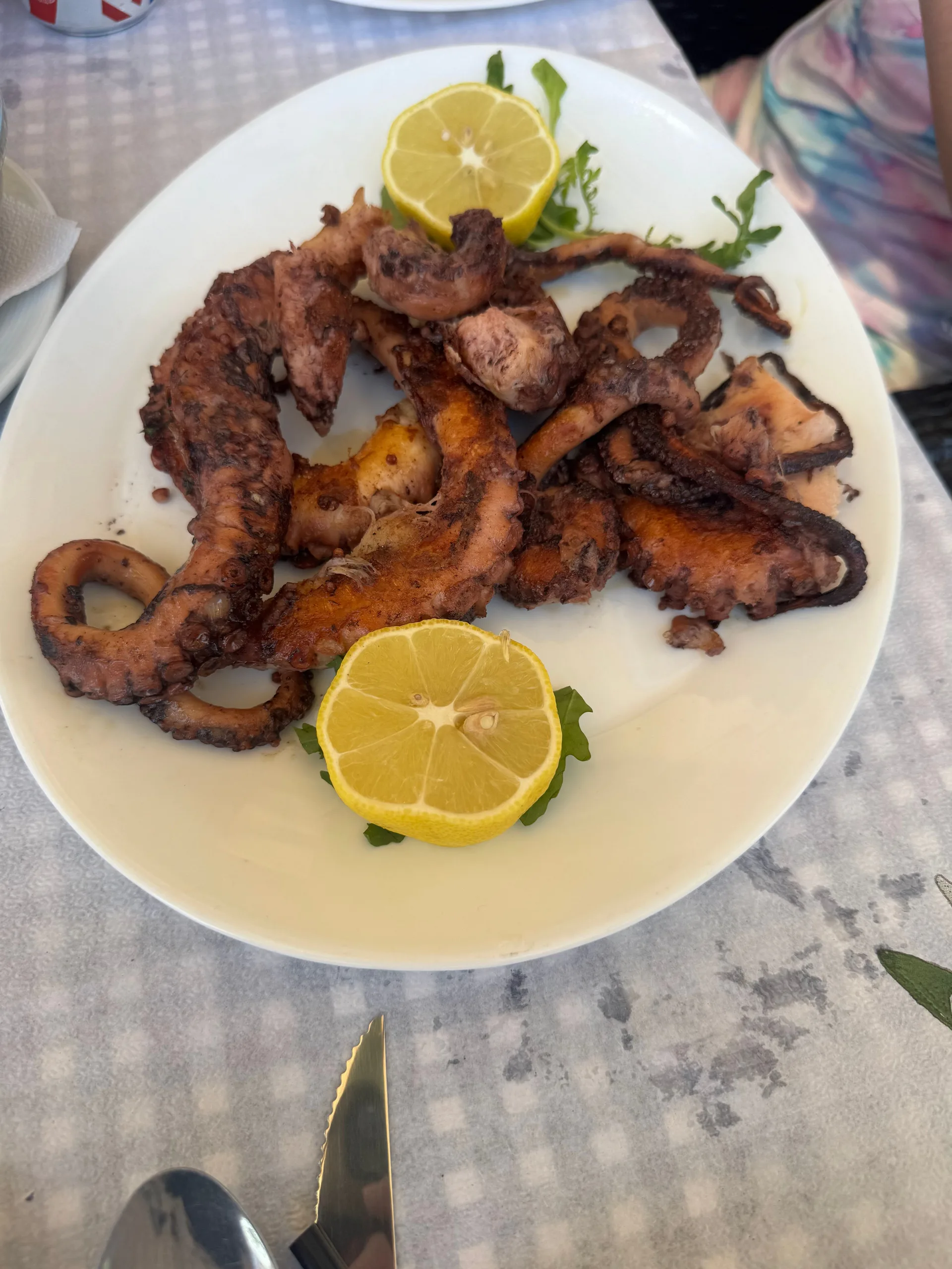 A plate of grilled octopus with lemon halves on a checked tablecloth