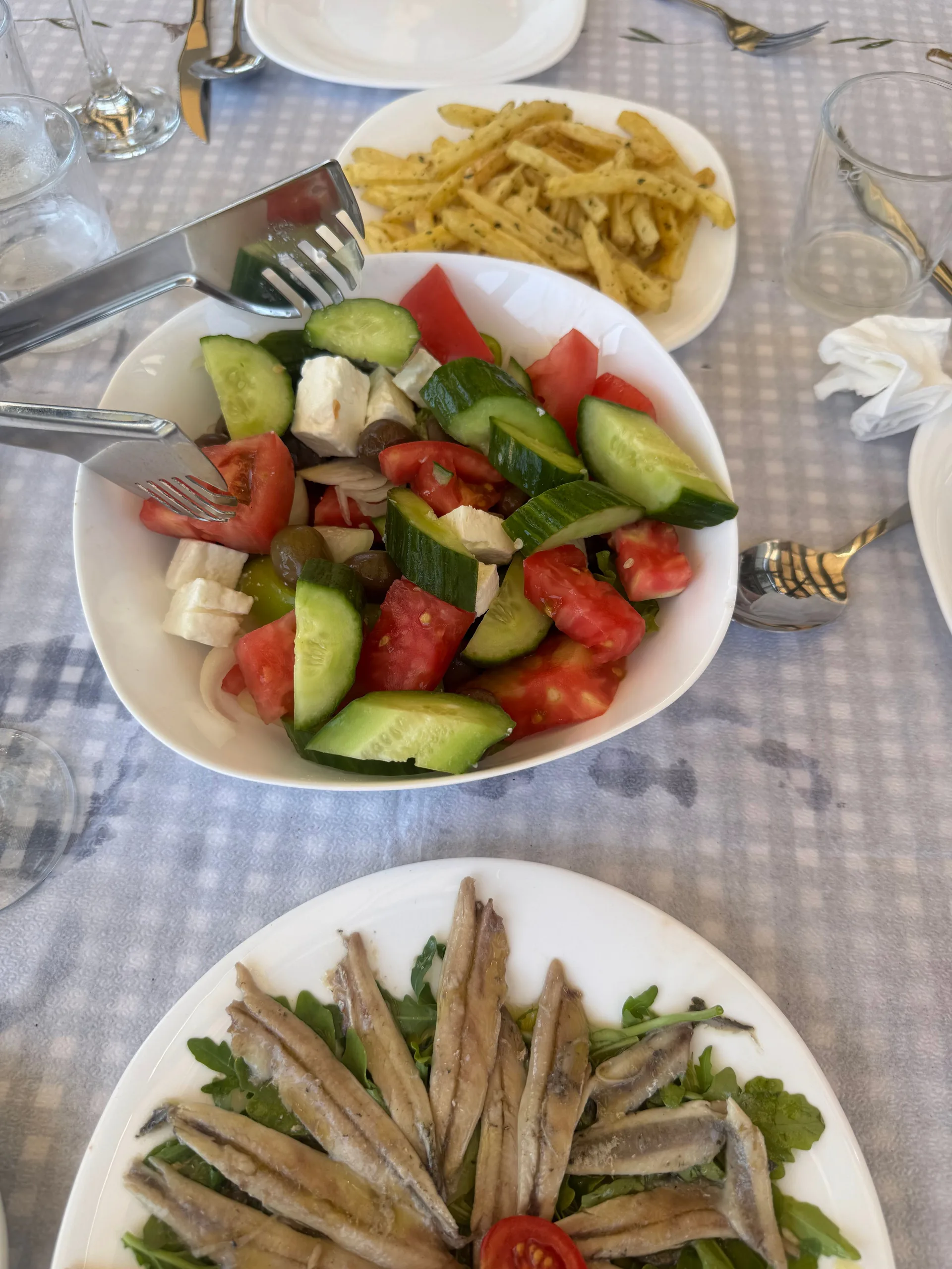 A Greek salad with feta beside a plate of marinated anchovies on rocket