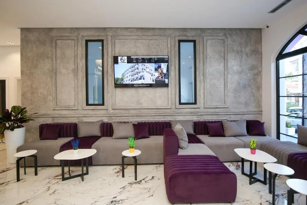 The lobby lounge at Chimaera Hotel with long low seating in grey and plum, small round tables and a panelled plaster wall