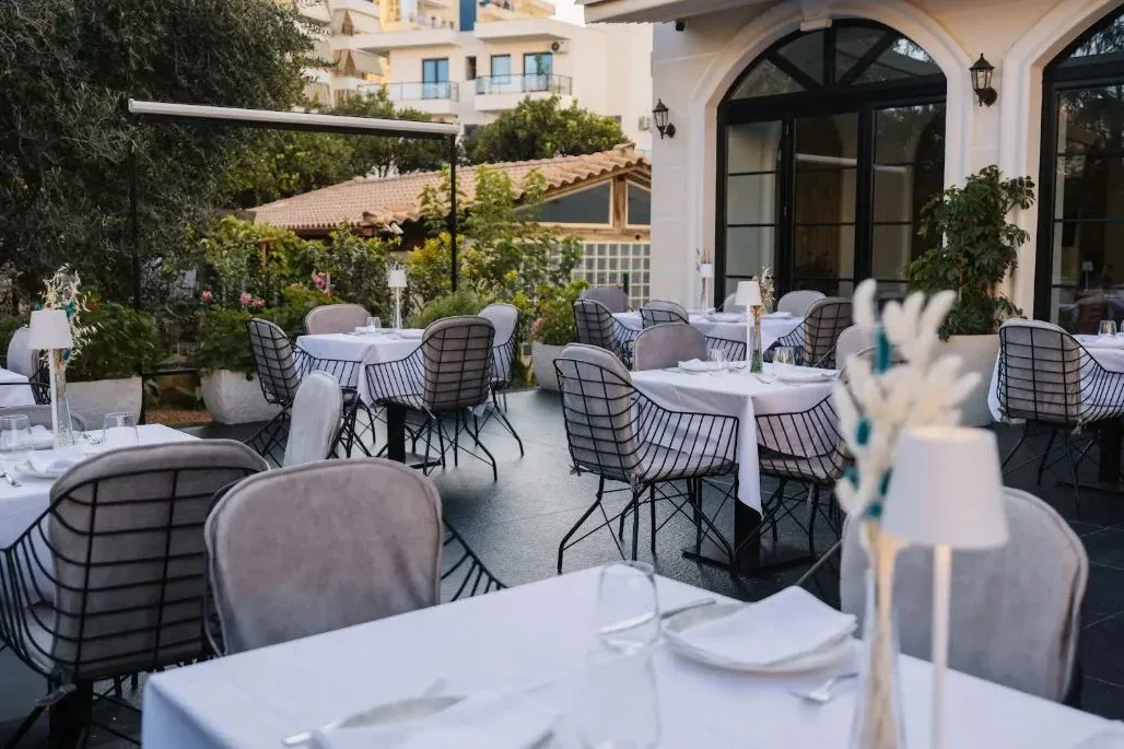 The restaurant terrace at Chimaera Hotel at dusk, laid tables under an awning beside the arched garden doors